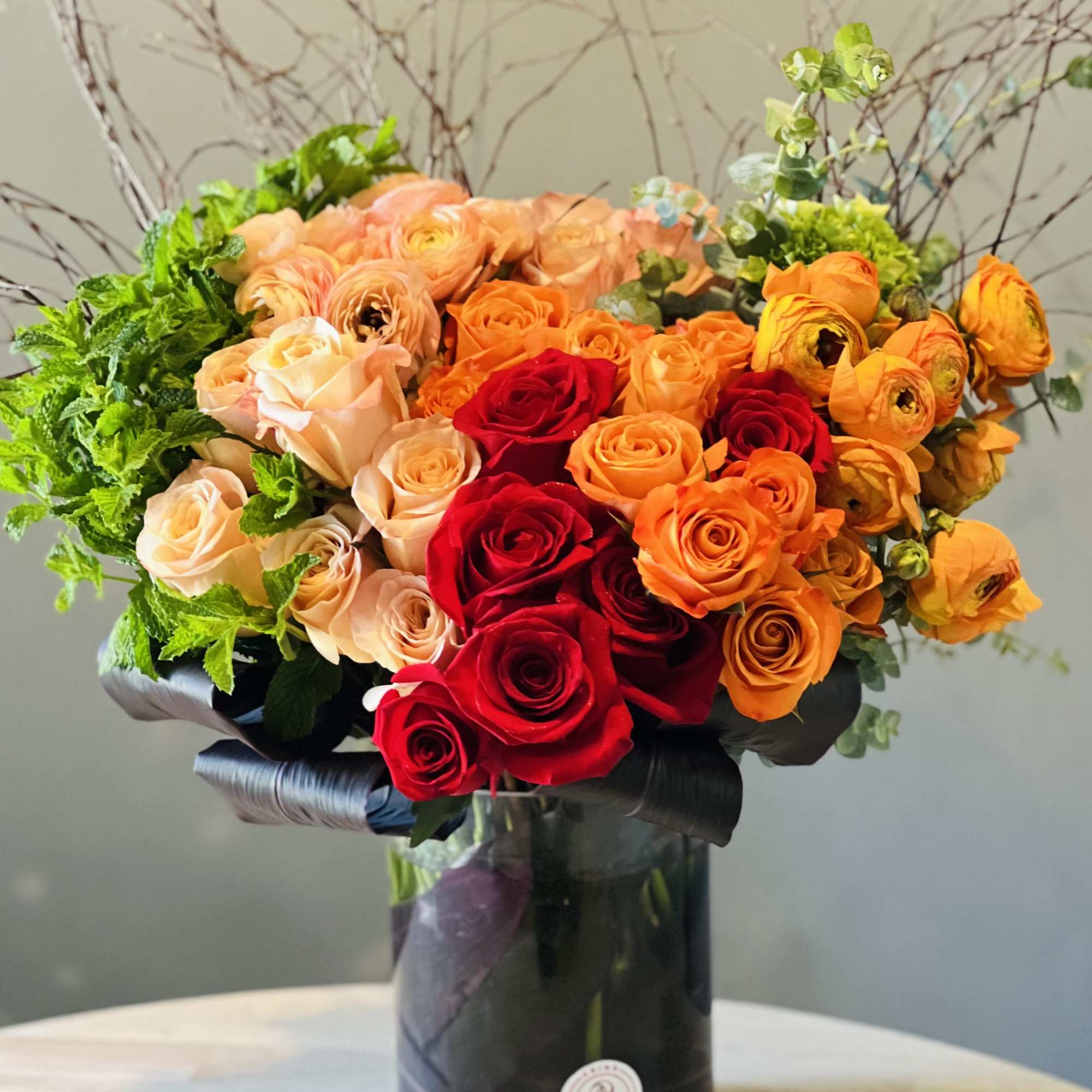 Bouquet of red, orange, and peach roses in a black vase