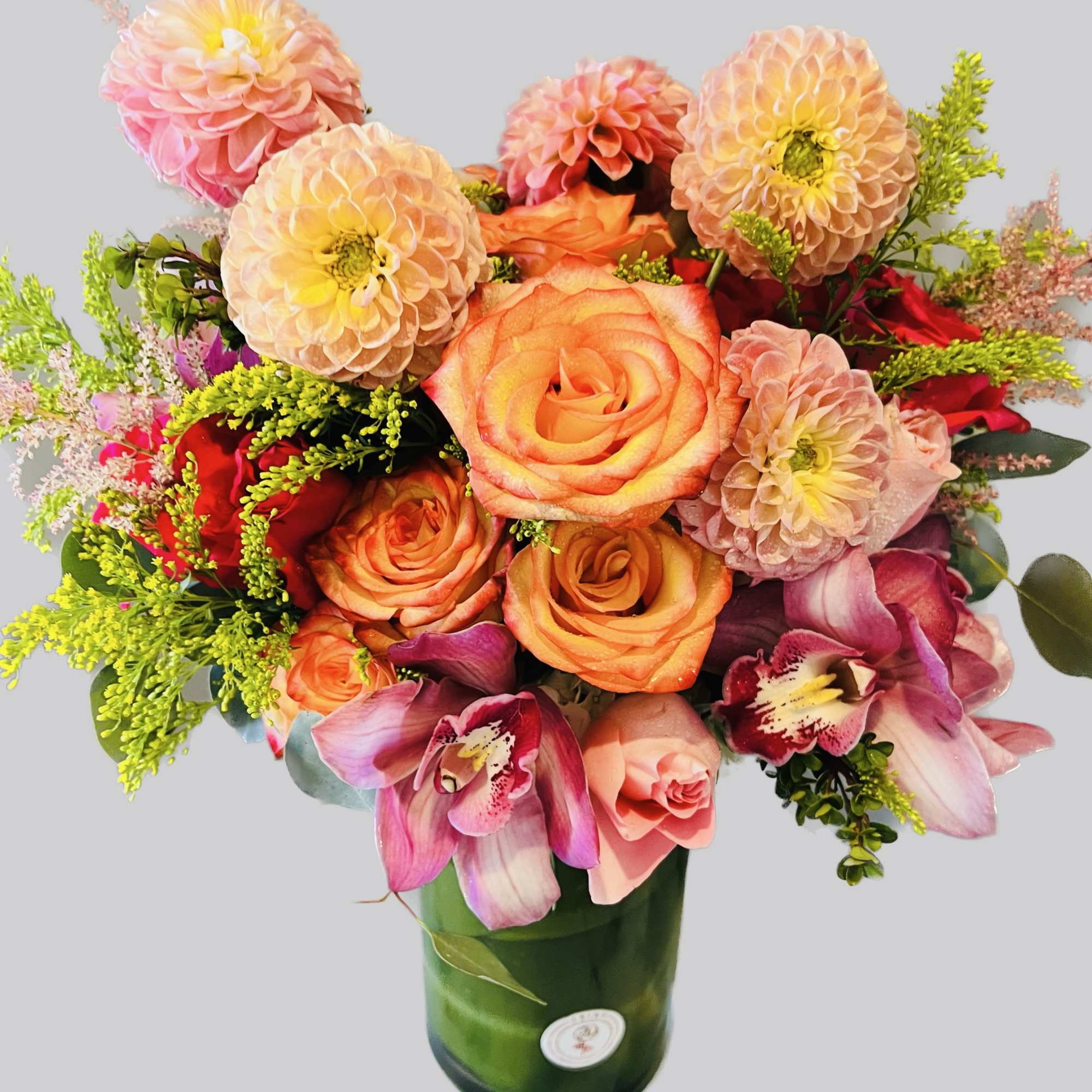 Bouquet of orange roses and pink dahlias in a green glass vase