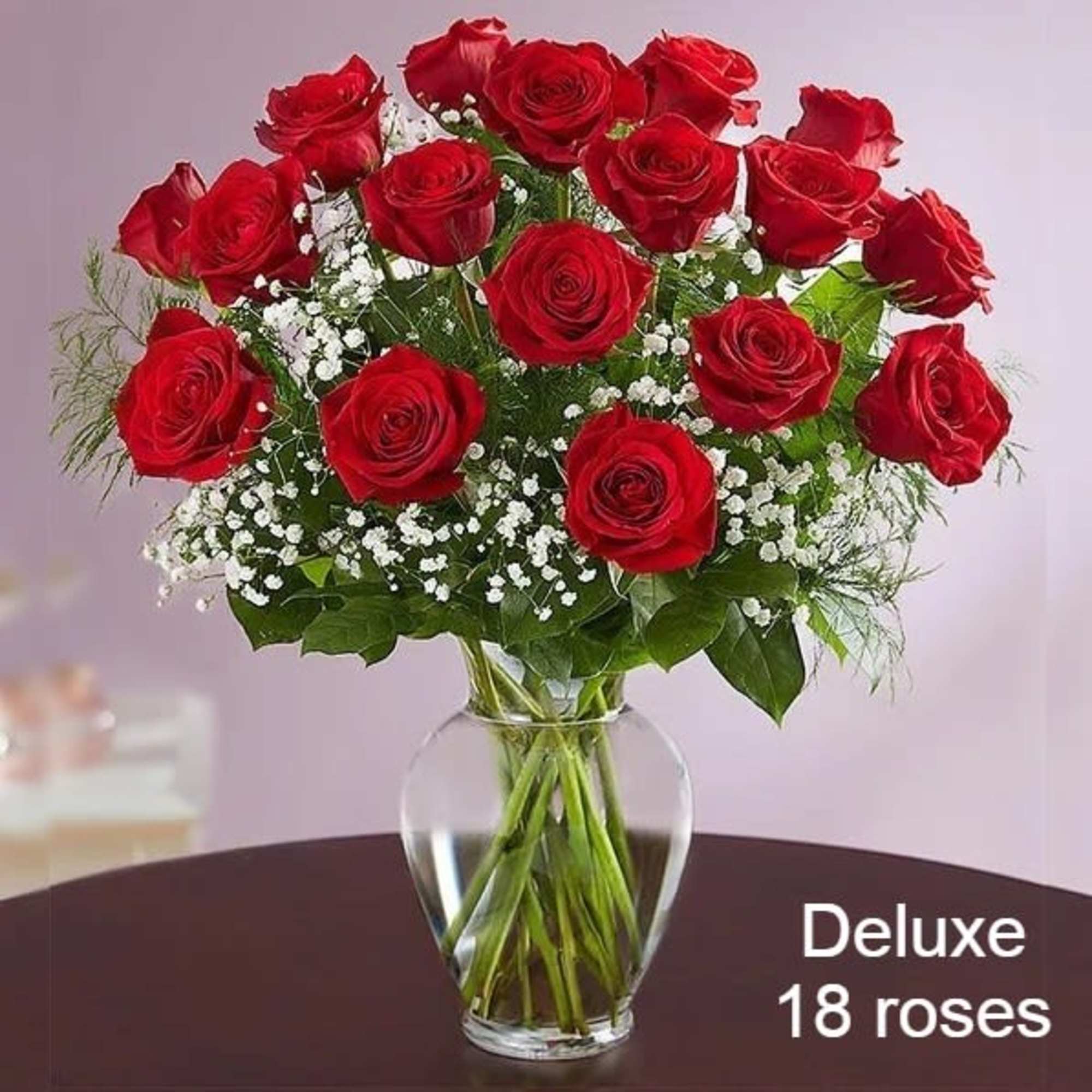 Arrangement of 18 red roses with white filler flowers in a clear glass vase on a table