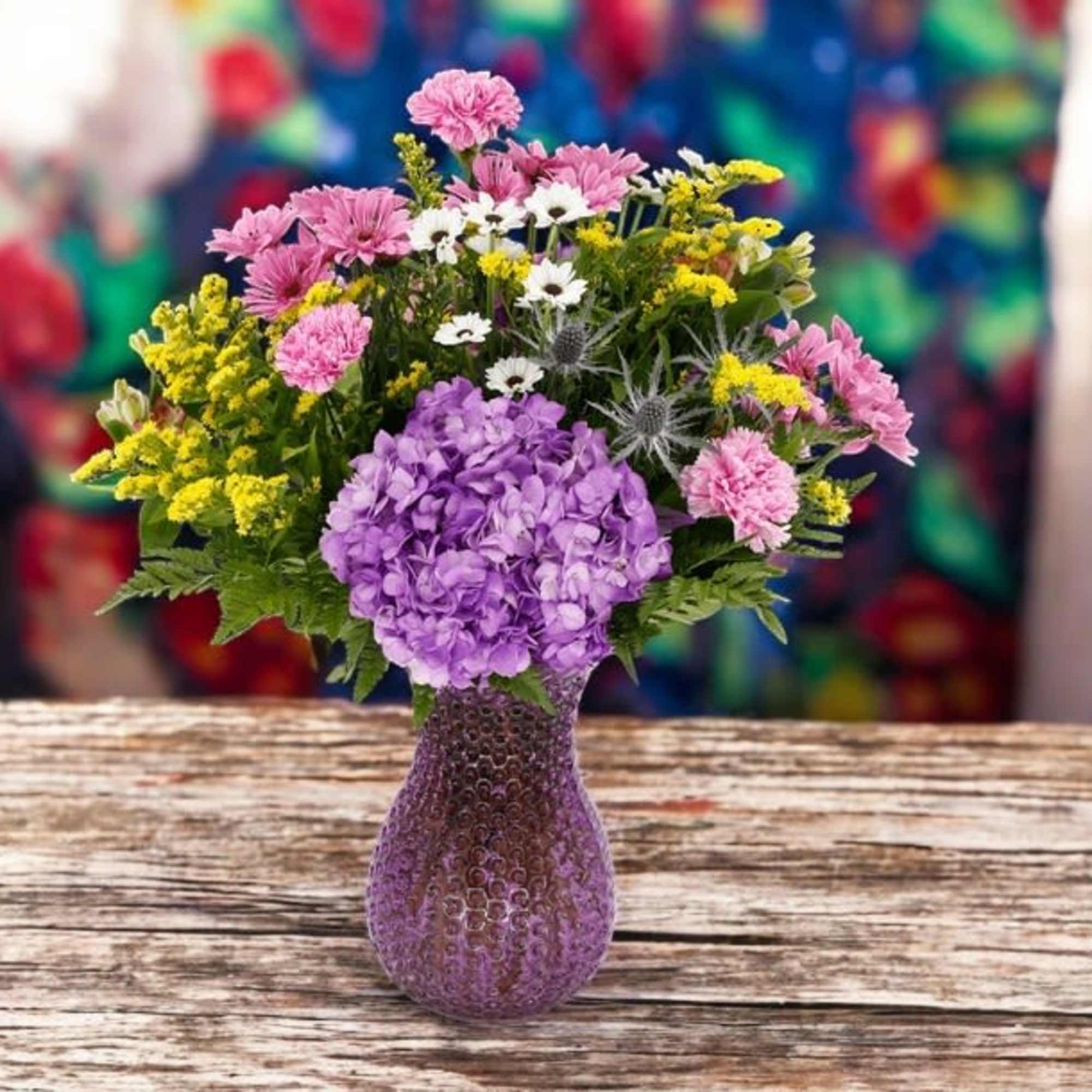 Mixed bouquet of purple, pink, white, and yellow flowers in a purple vase