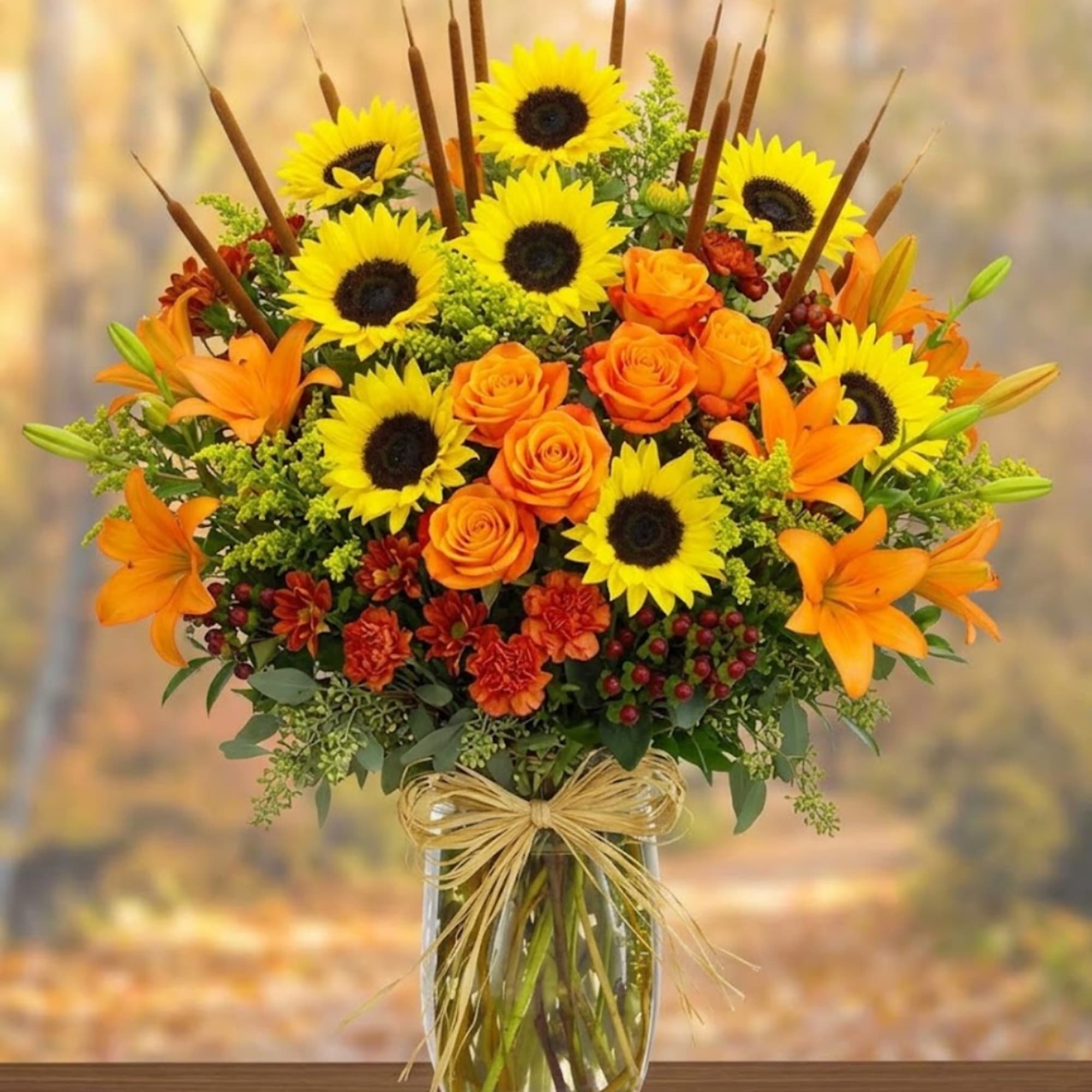 Sunflower and orange rose arrangement in a clear glass vase with a raffia bow
