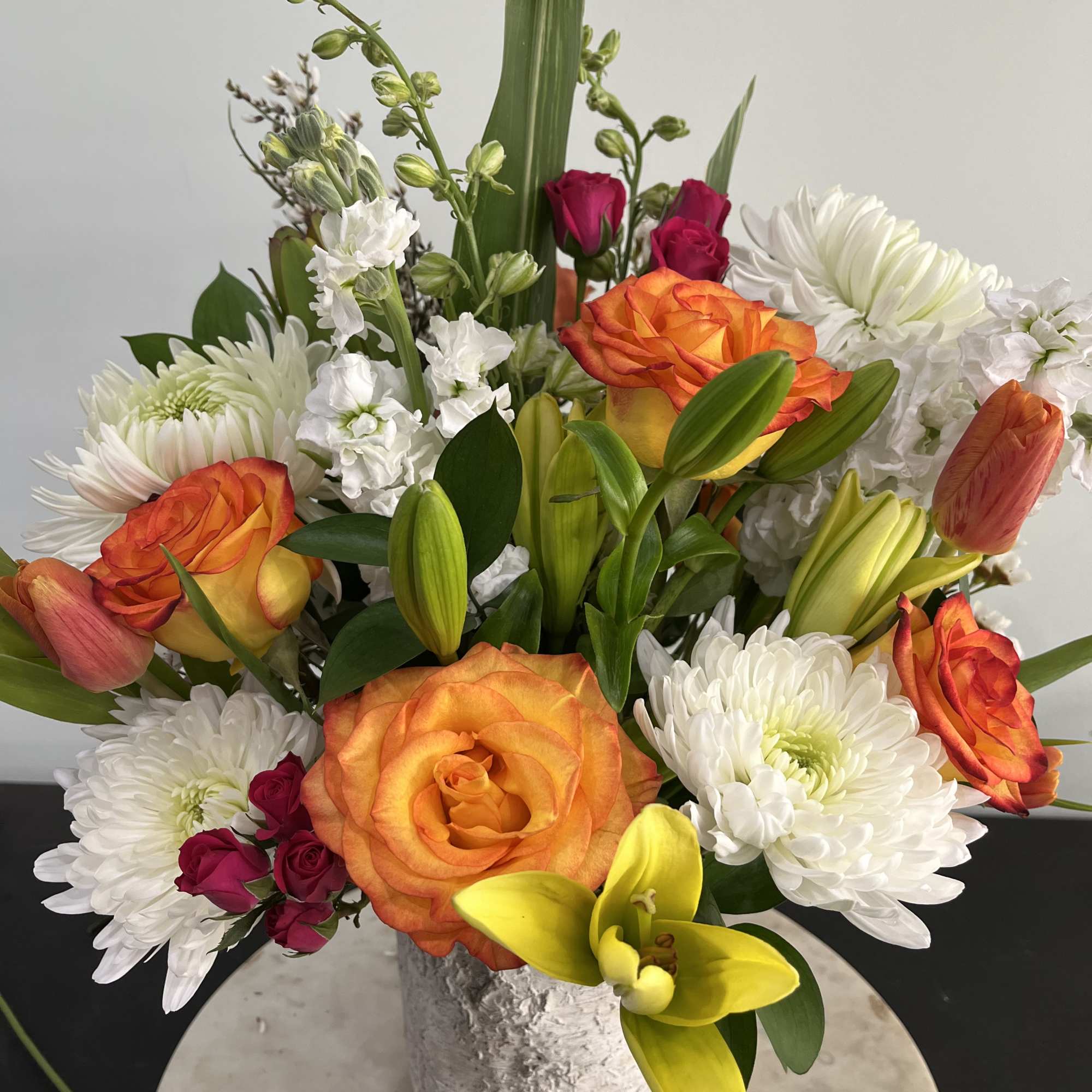 Mixed bouquet of orange roses, white chrysanthemums, and yellow lilies in a textured vase