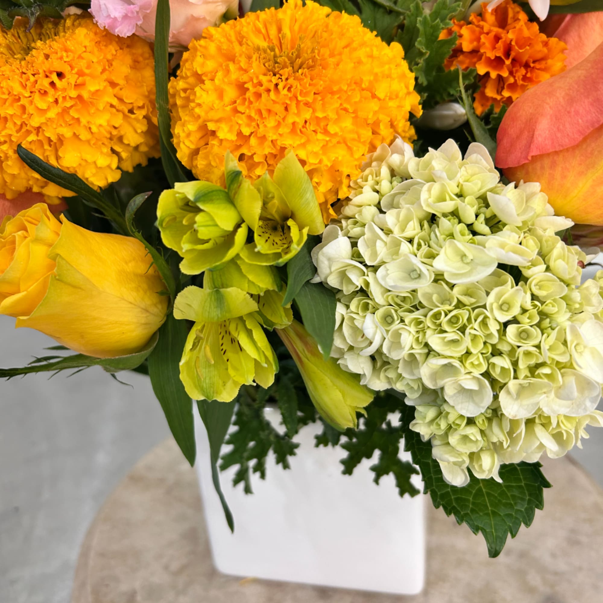 Bright yellow and orange bouquet with roses and hydrangeas in a white vase