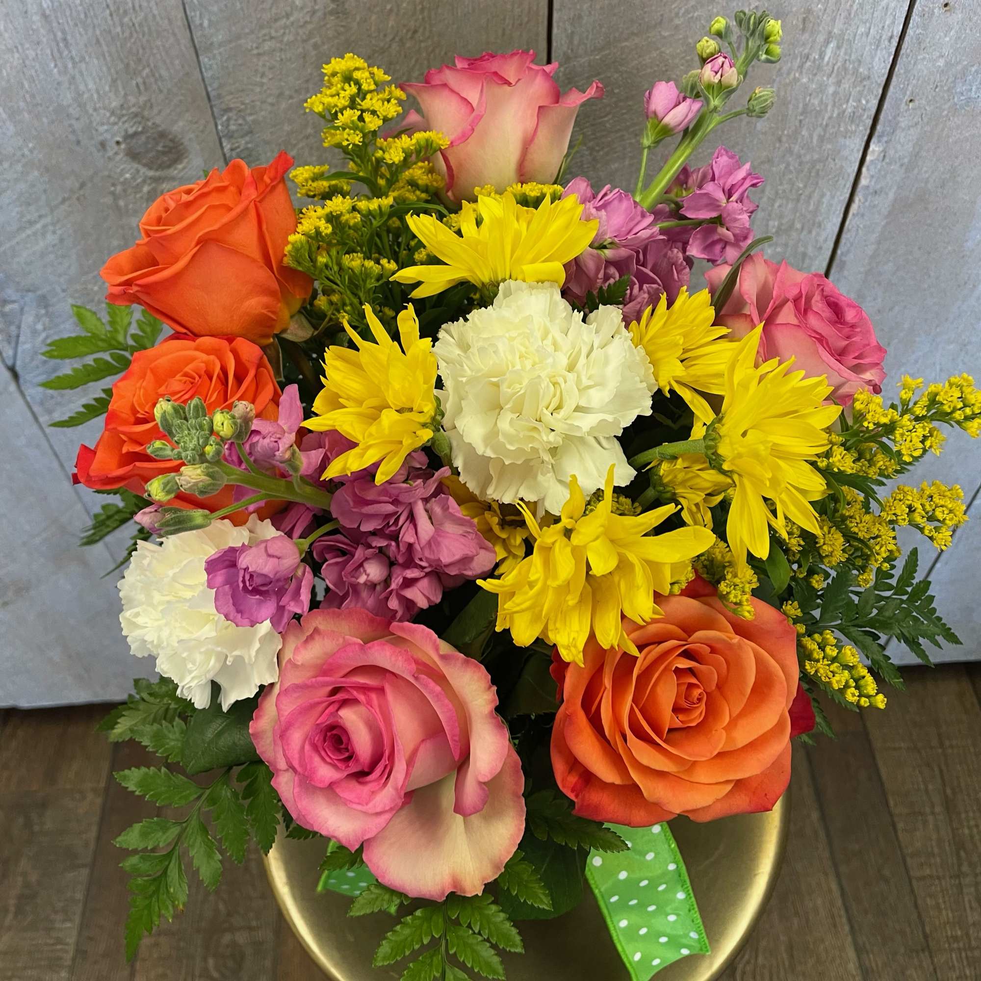 Mixed bouquet of roses, carnations, and yellow daisies in a gold vase