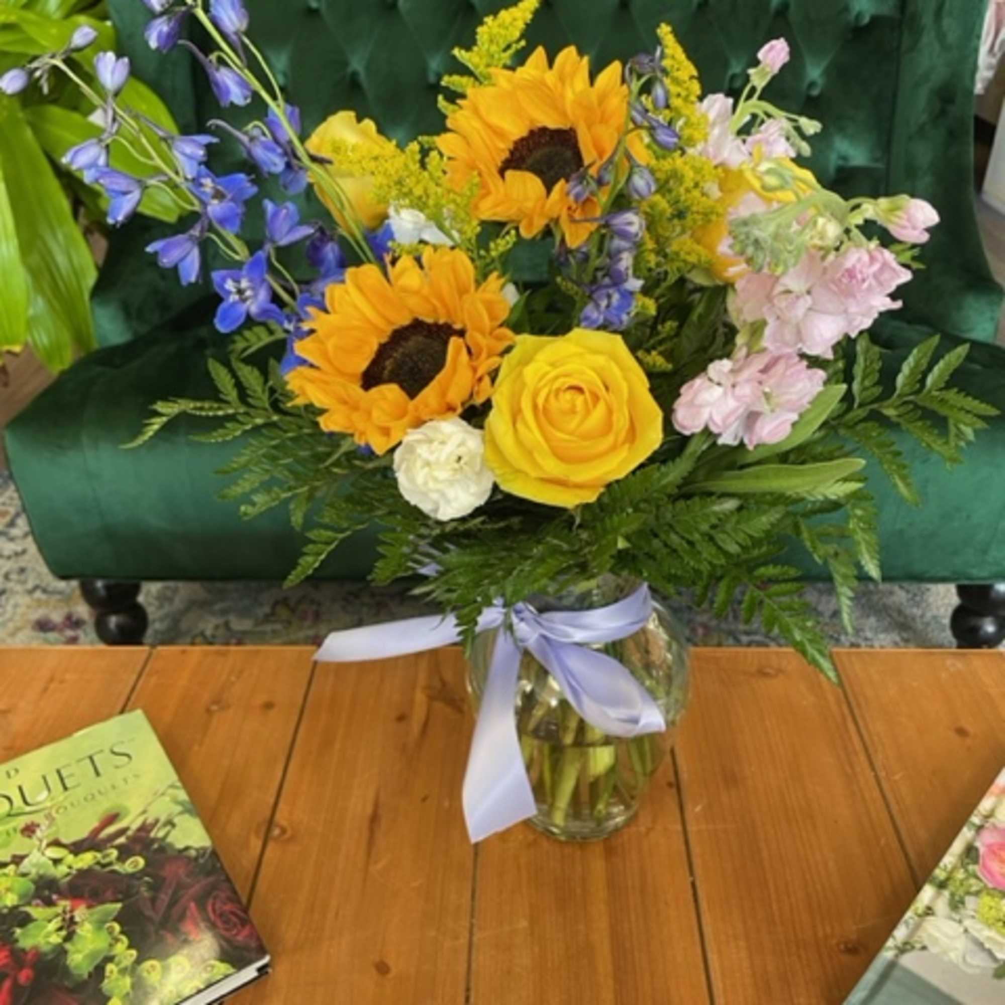 Bouquet of sunflowers, yellow roses, and blue flowers in a glass vase