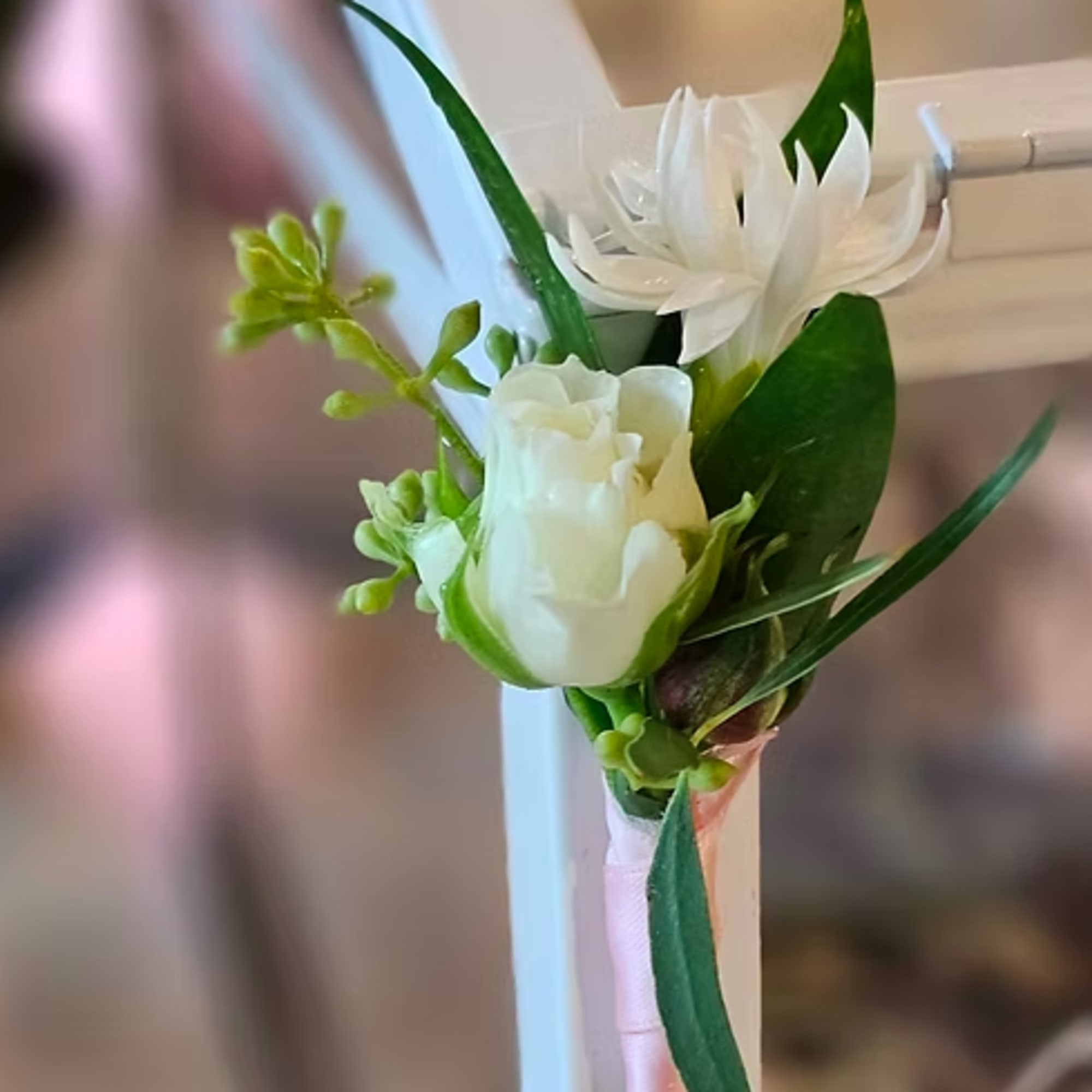 White floral boutonniere with green accents and a pale ribbon