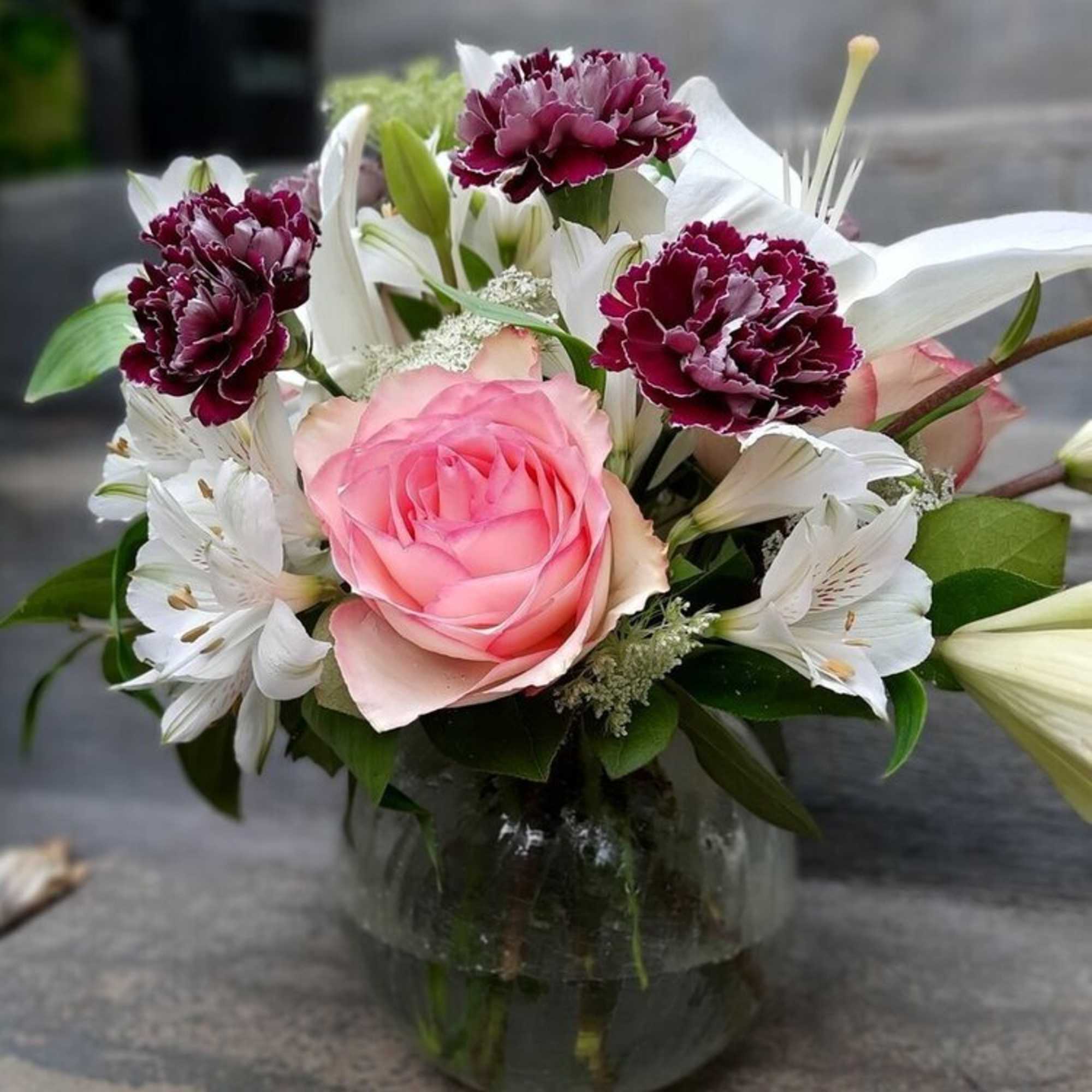 Pink rose bouquet with white lilies and burgundy carnations in a glass vase