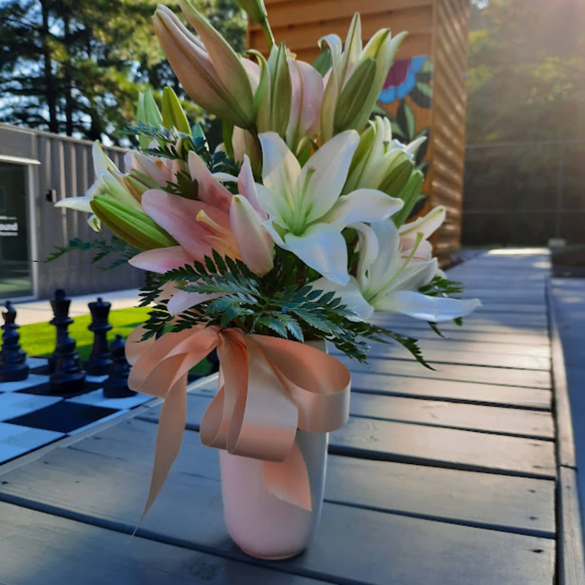 Pink and white lilies arranged in a vase with a ribbon bow