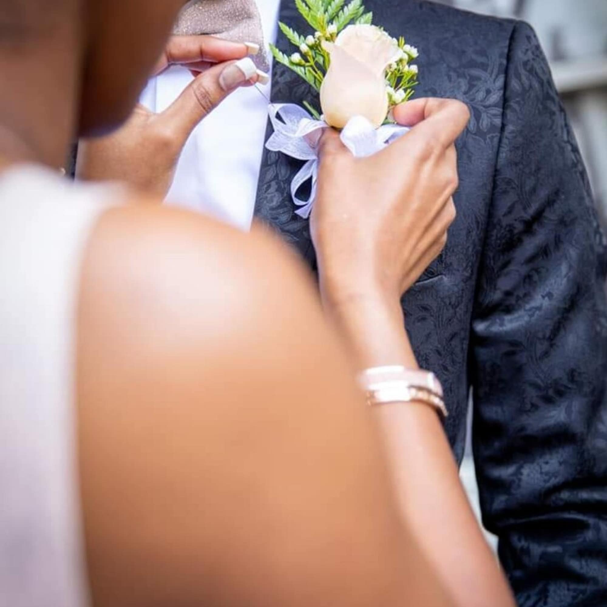 Person pinning a white rose boutonniere onto a man's suit jacket