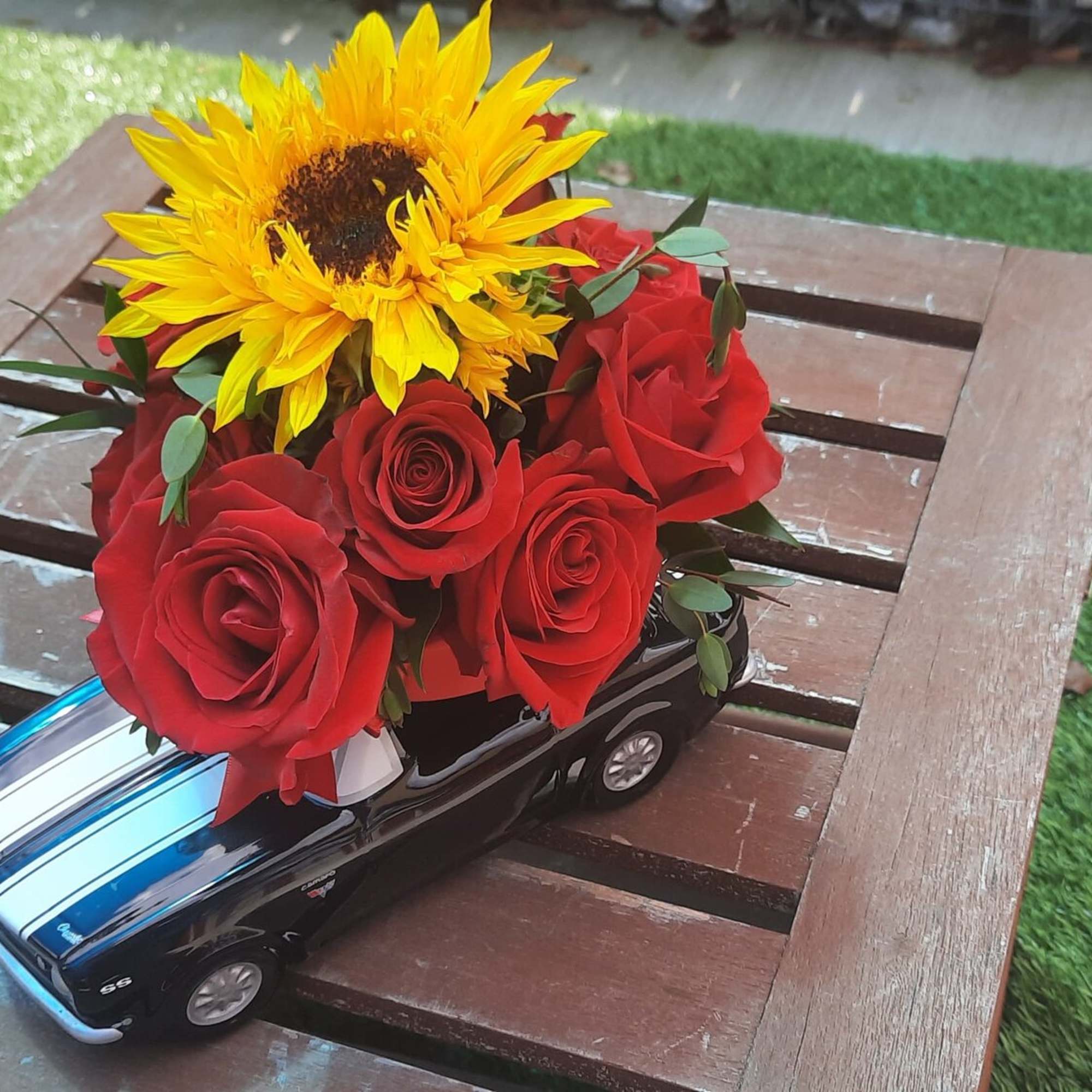 Red roses and a sunflower arranged on a toy car