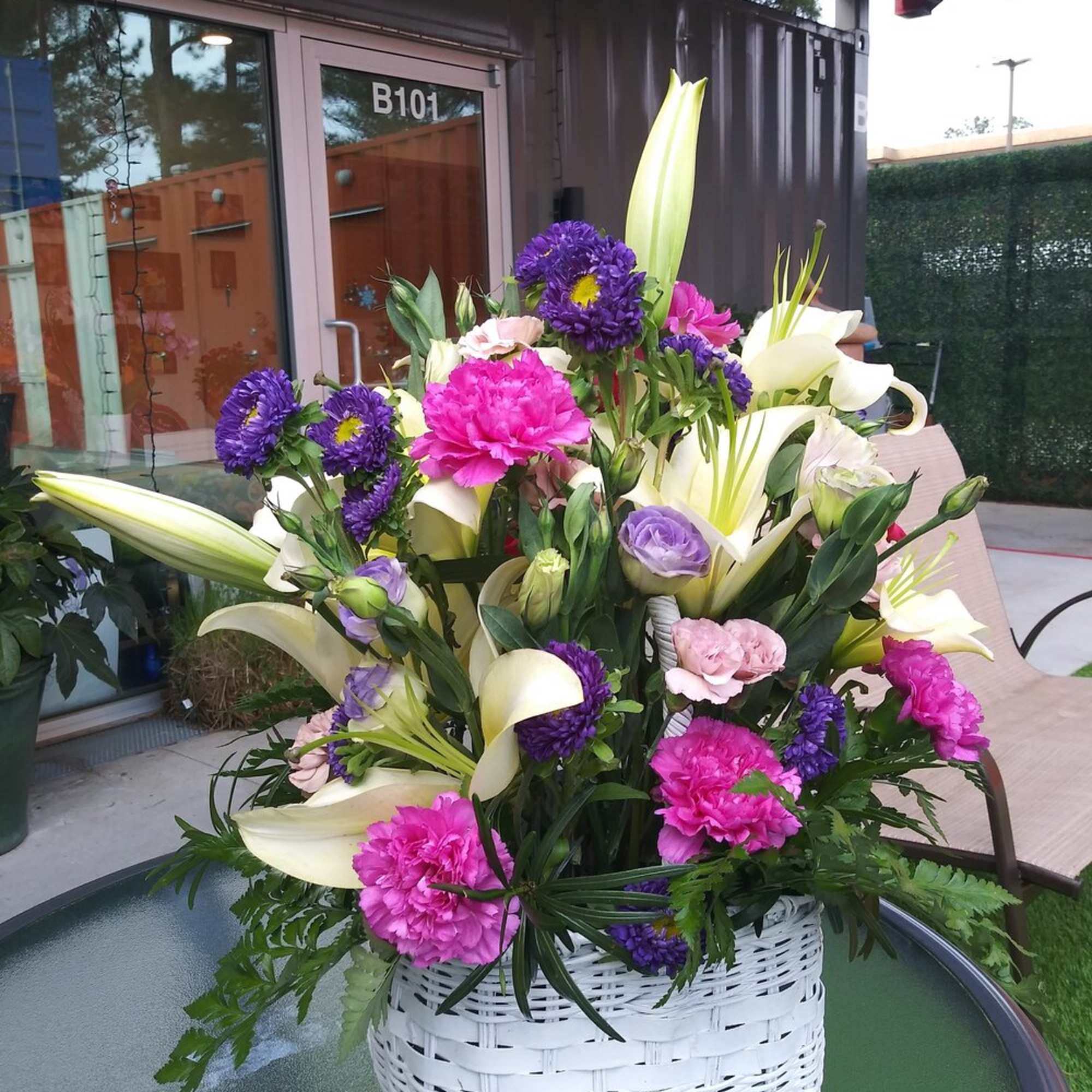 Basket arrangement with white lilies, pink carnations, and purple flowers