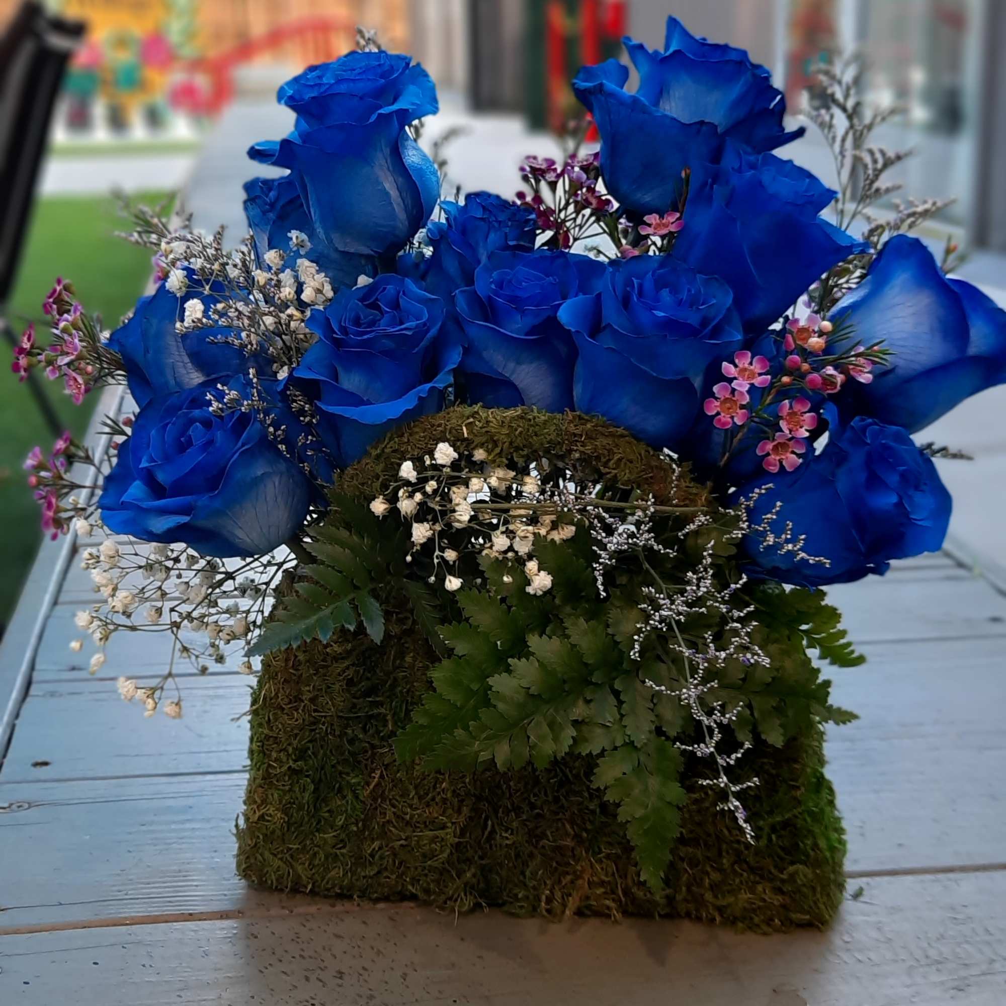 Blue roses arranged in a moss-covered container with small filler flowers.