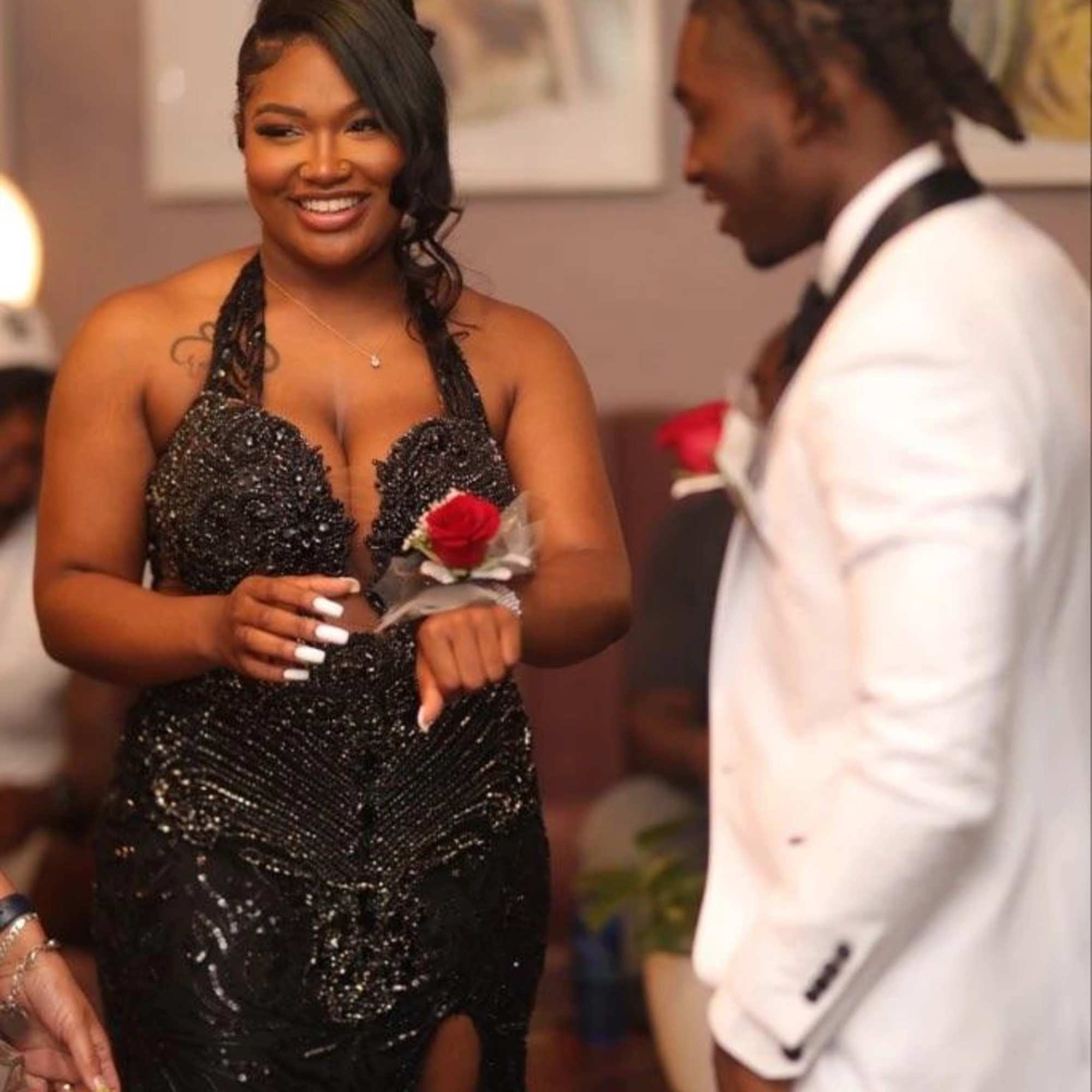 Woman in a black dress wearing a red rose corsage beside a man in a white tuxedo