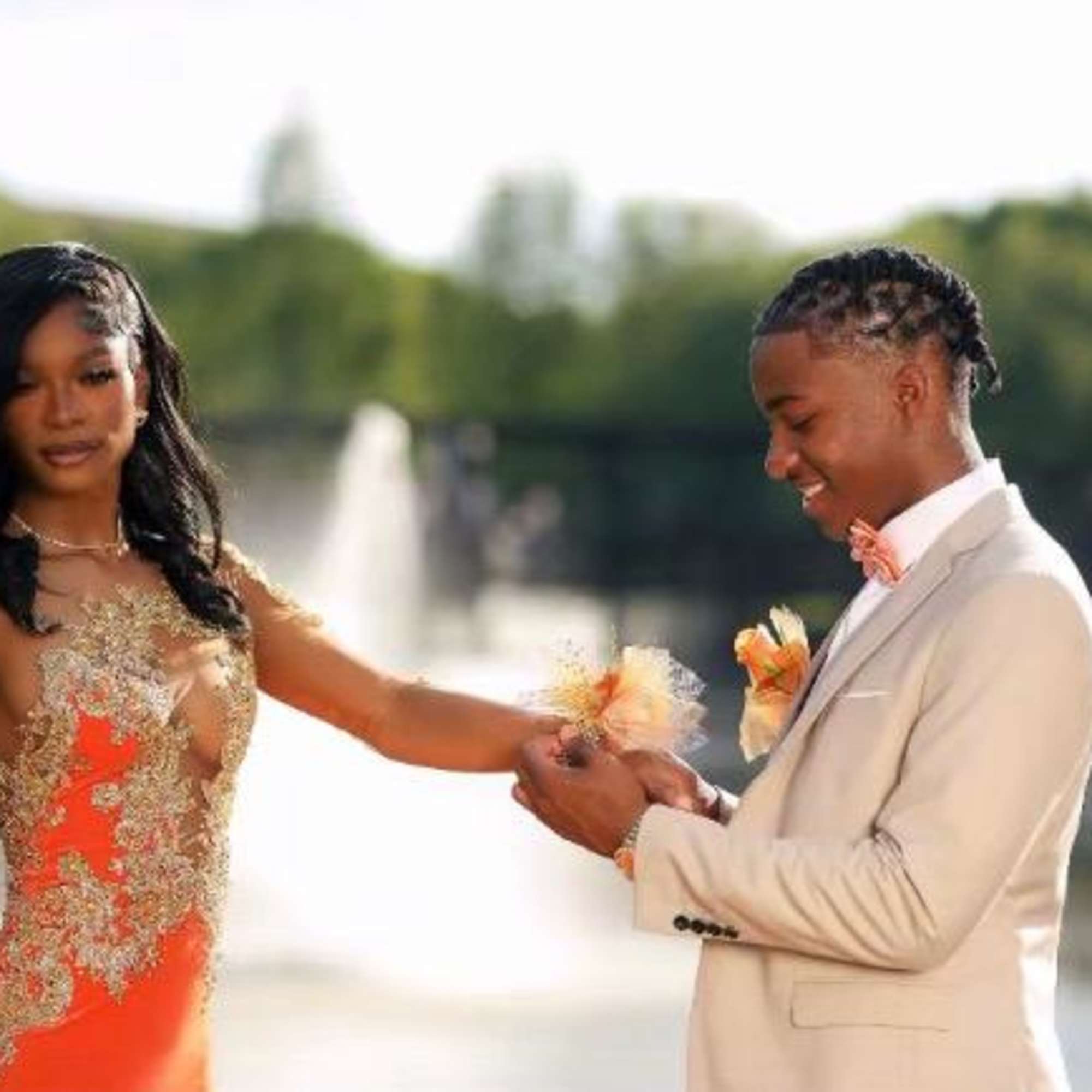 A young couple in formal attire stands by a fountain outdoors