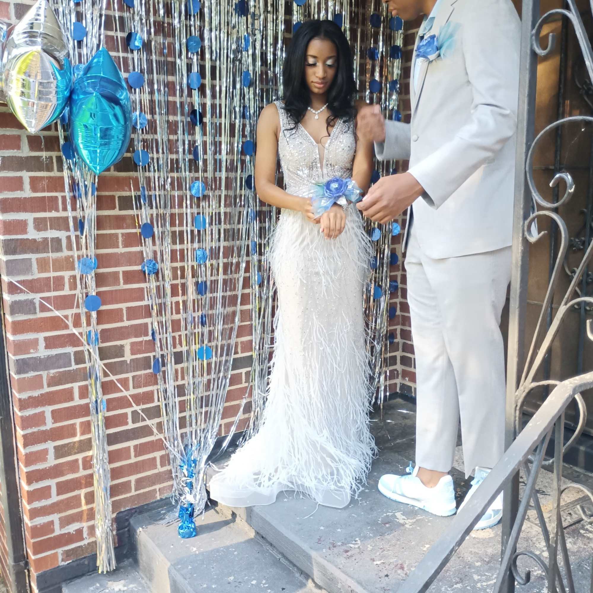 Couple in formal attire at a blue-and-silver decorated entrance with balloons and streamers.