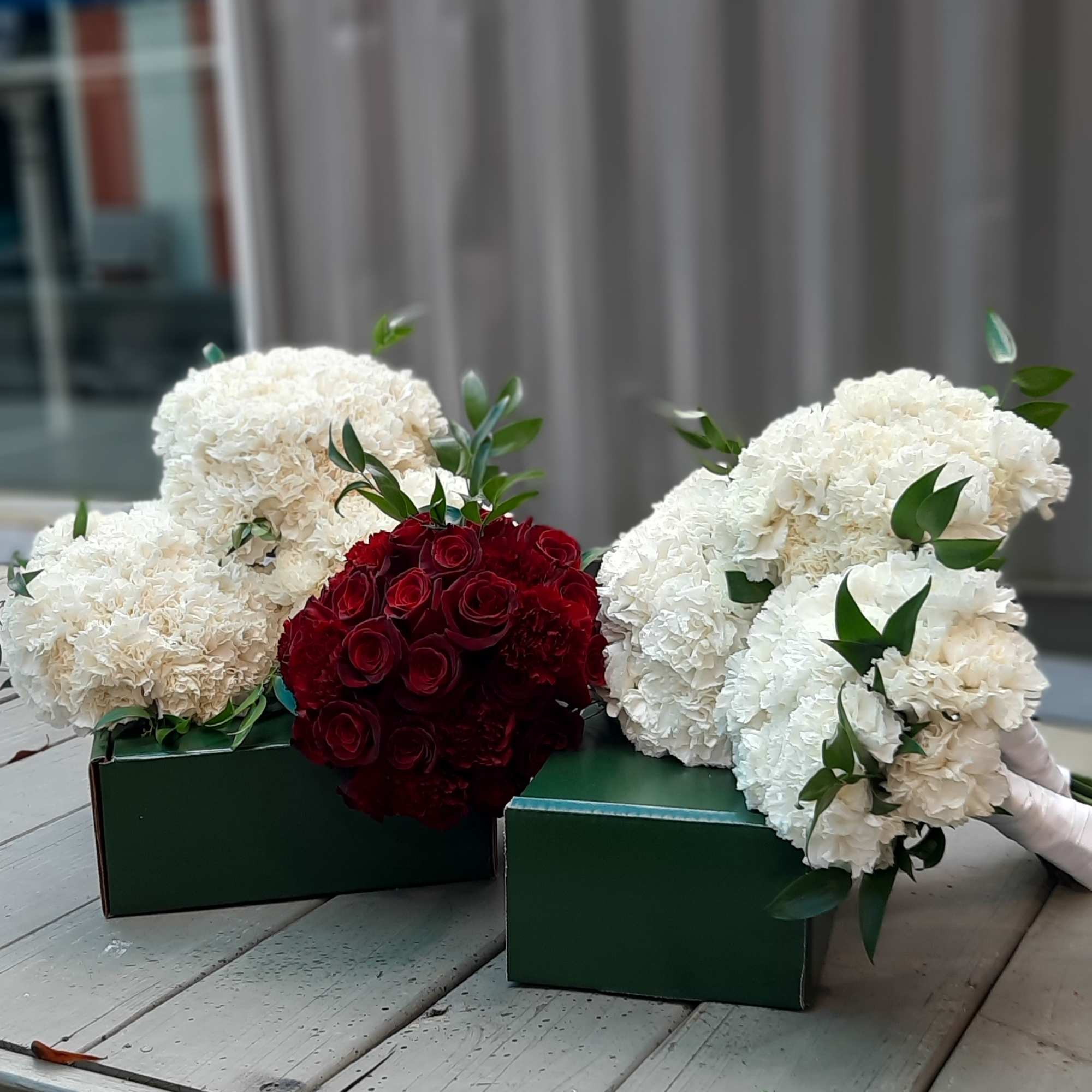 Bouquets of white carnations and red roses in green boxes