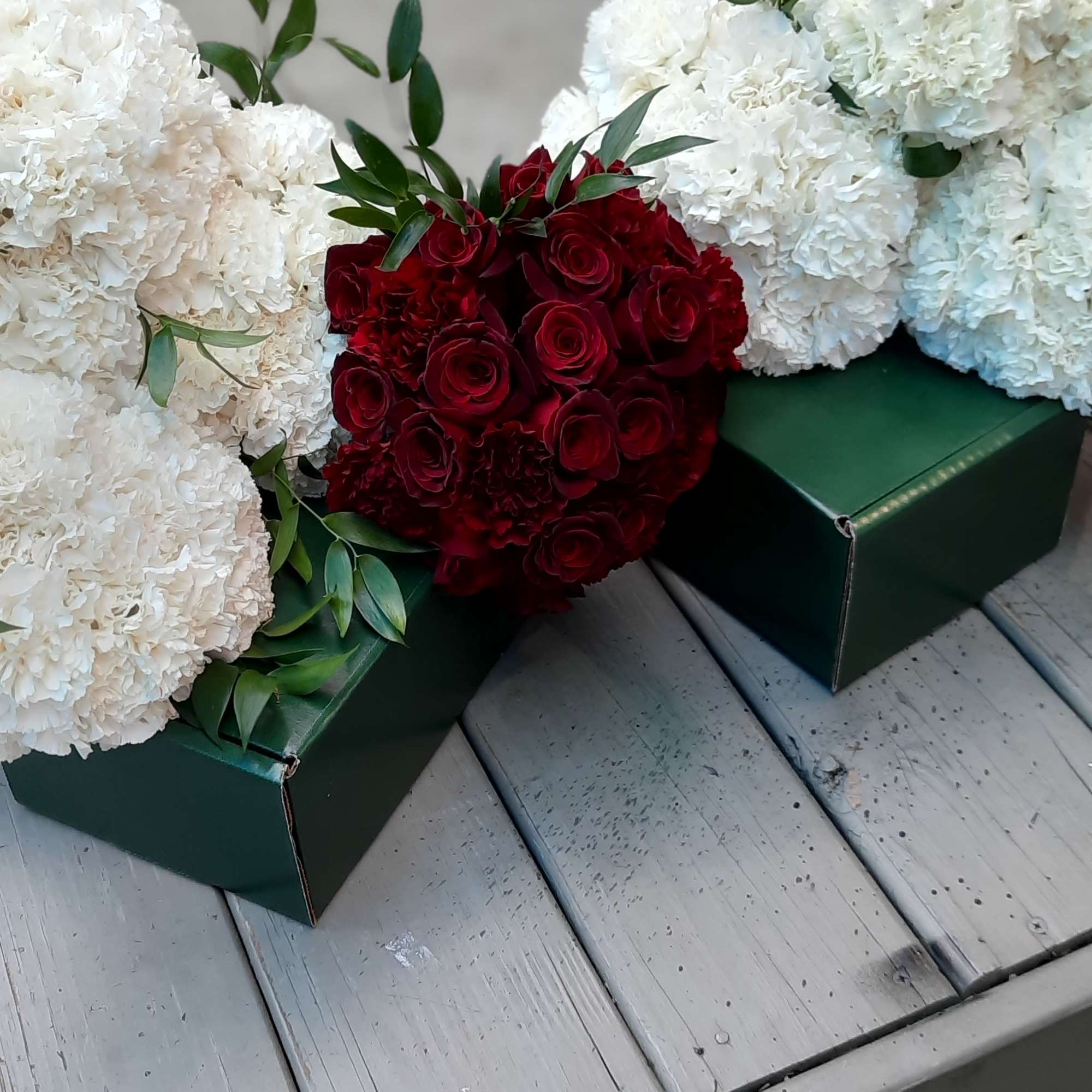 White carnation arrangements with a red rose bouquet in green boxes