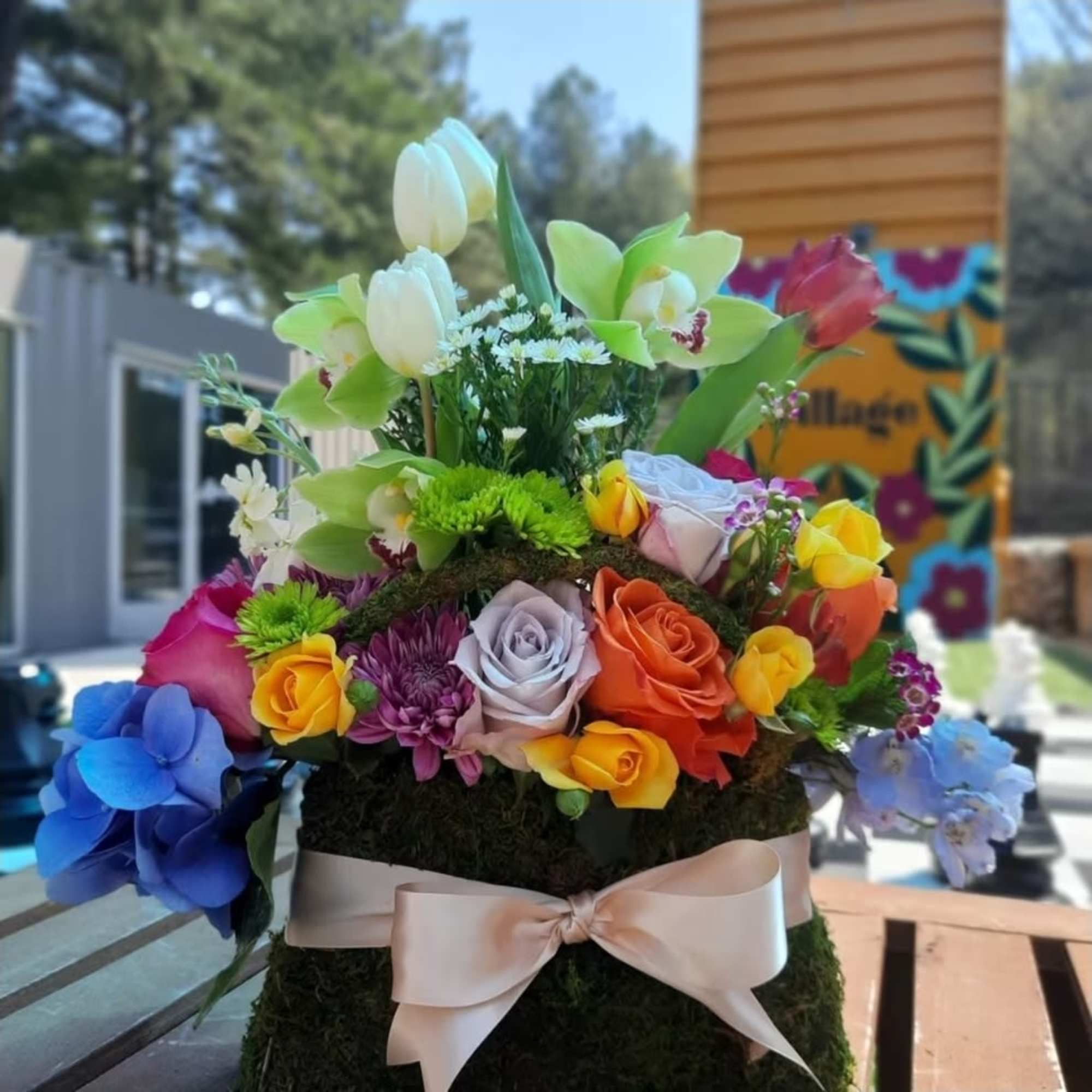 Colorful mixed flower arrangement with roses and orchids on a moss-covered base