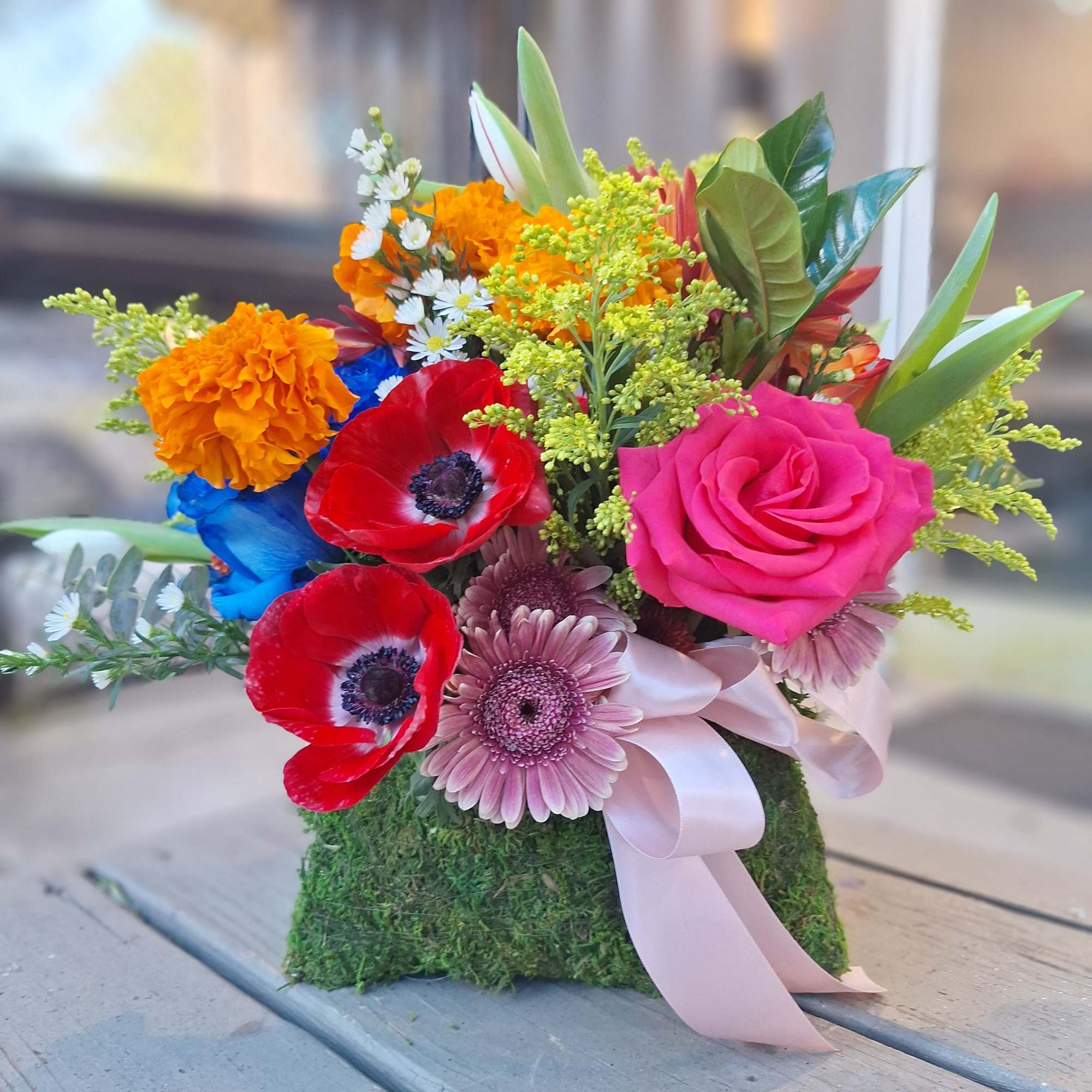 Bright mixed bouquet with roses, gerbera daisies, and marigolds in a moss-covered base