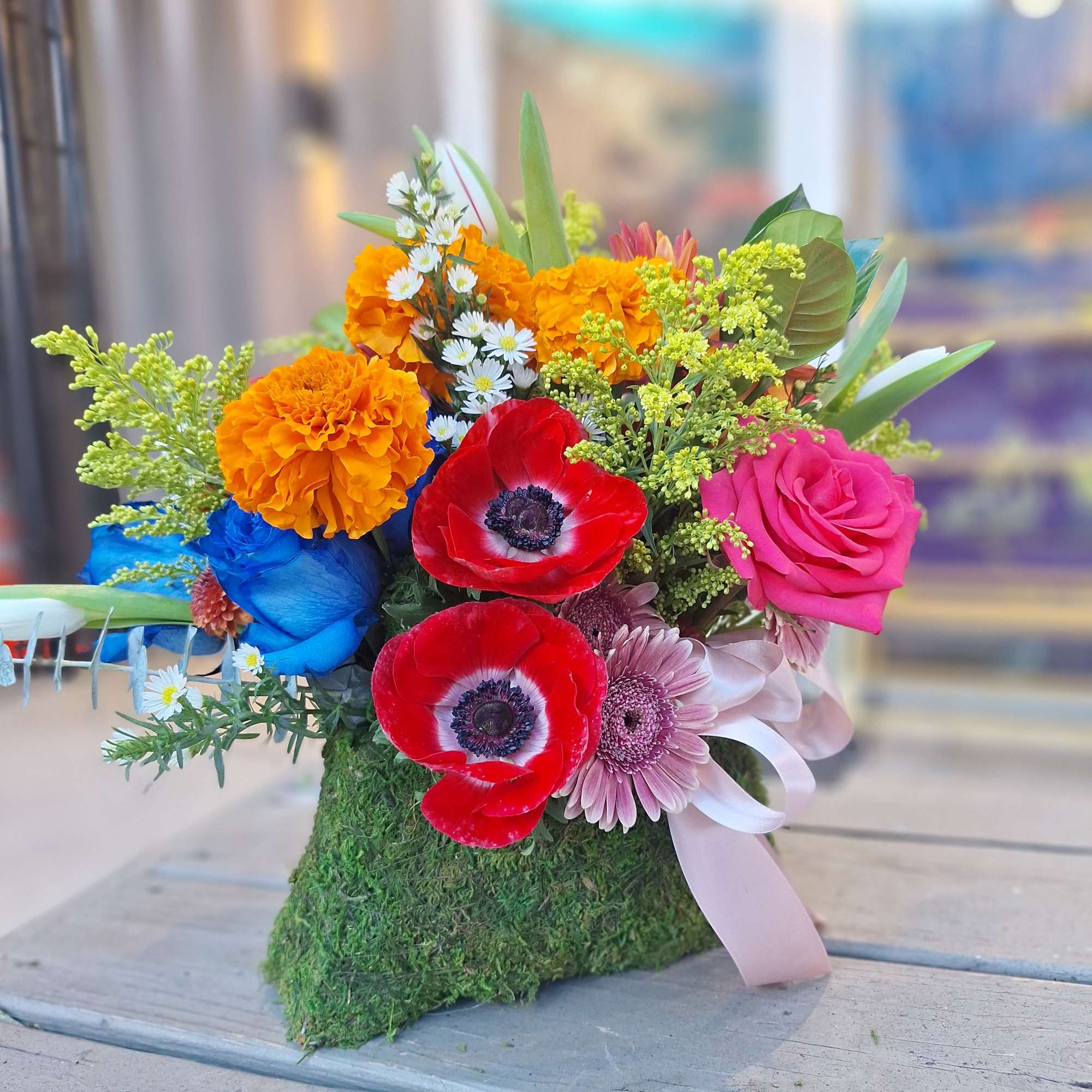 Colorful bouquet with red anemones, pink rose, orange marigolds, and blue blooms