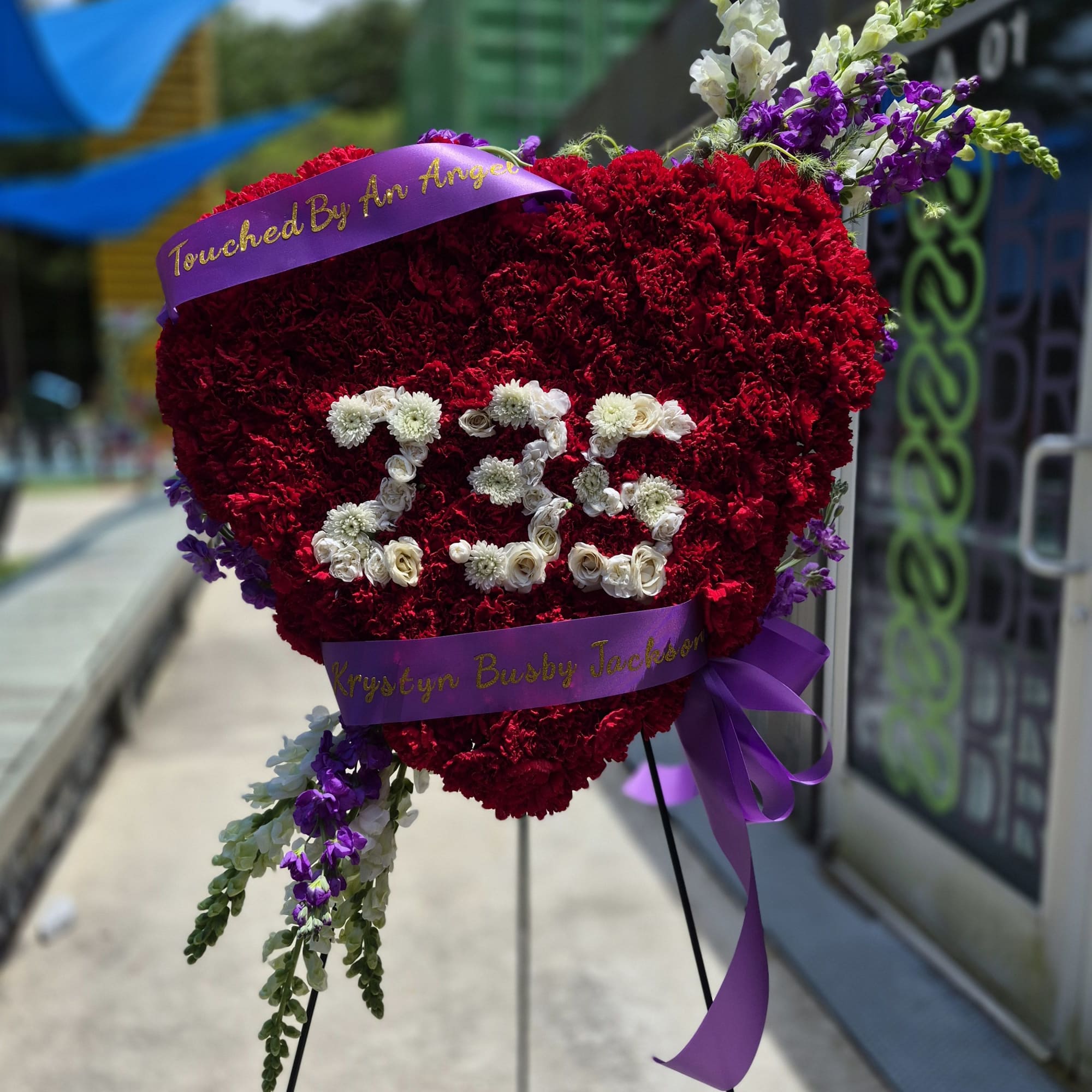 A closed heart wreath with red carnations and clusters of red roses