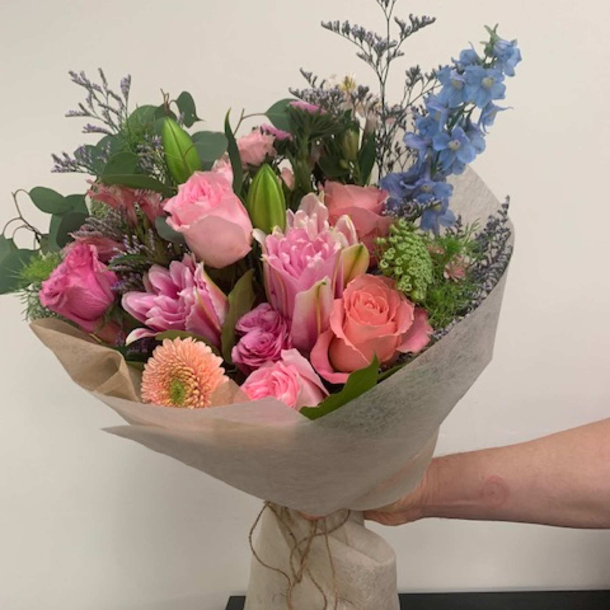 Hand-tied bouquet of pink and blue flowers wrapped in paper
