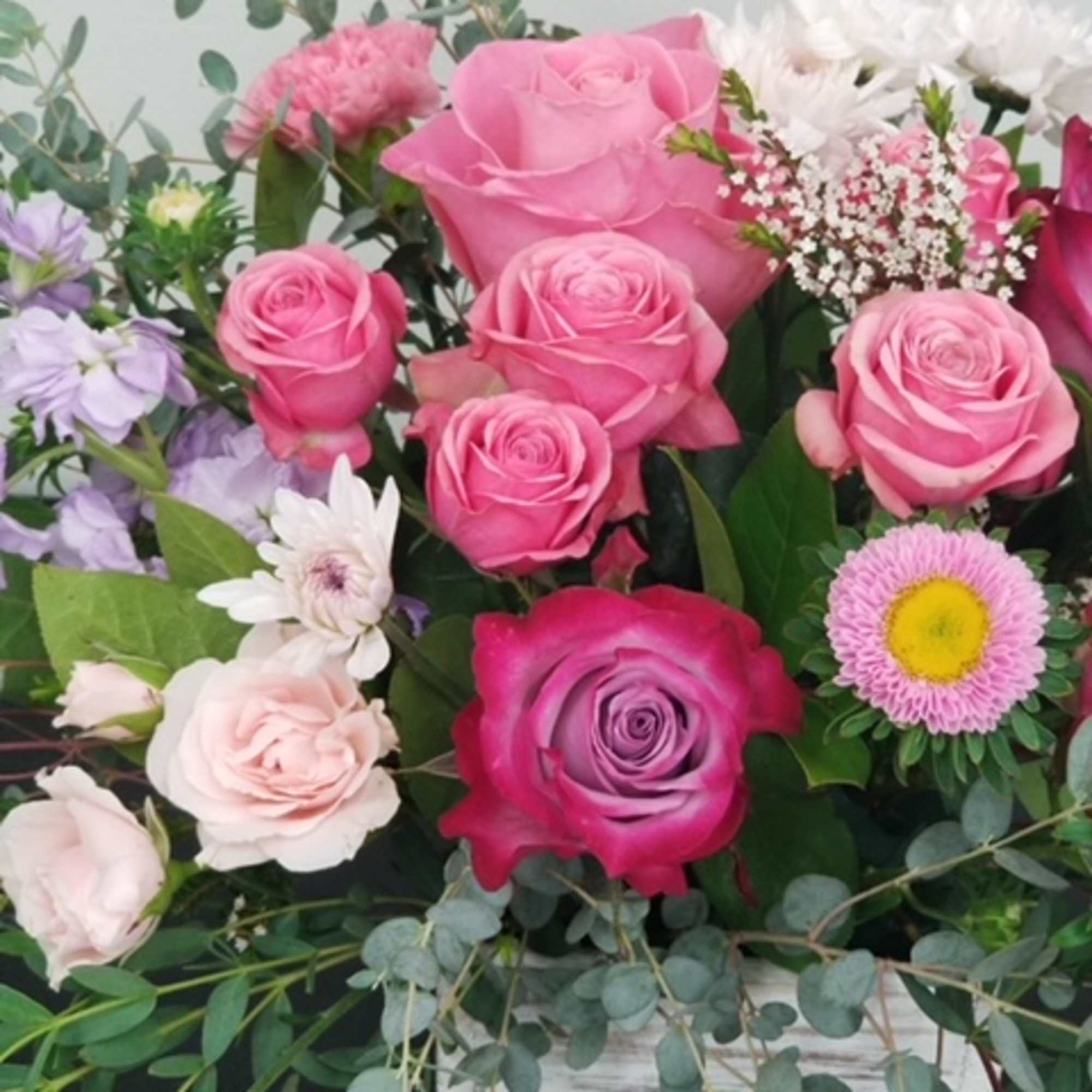Pink roses and mixed flowers arranged with eucalyptus in a rustic container