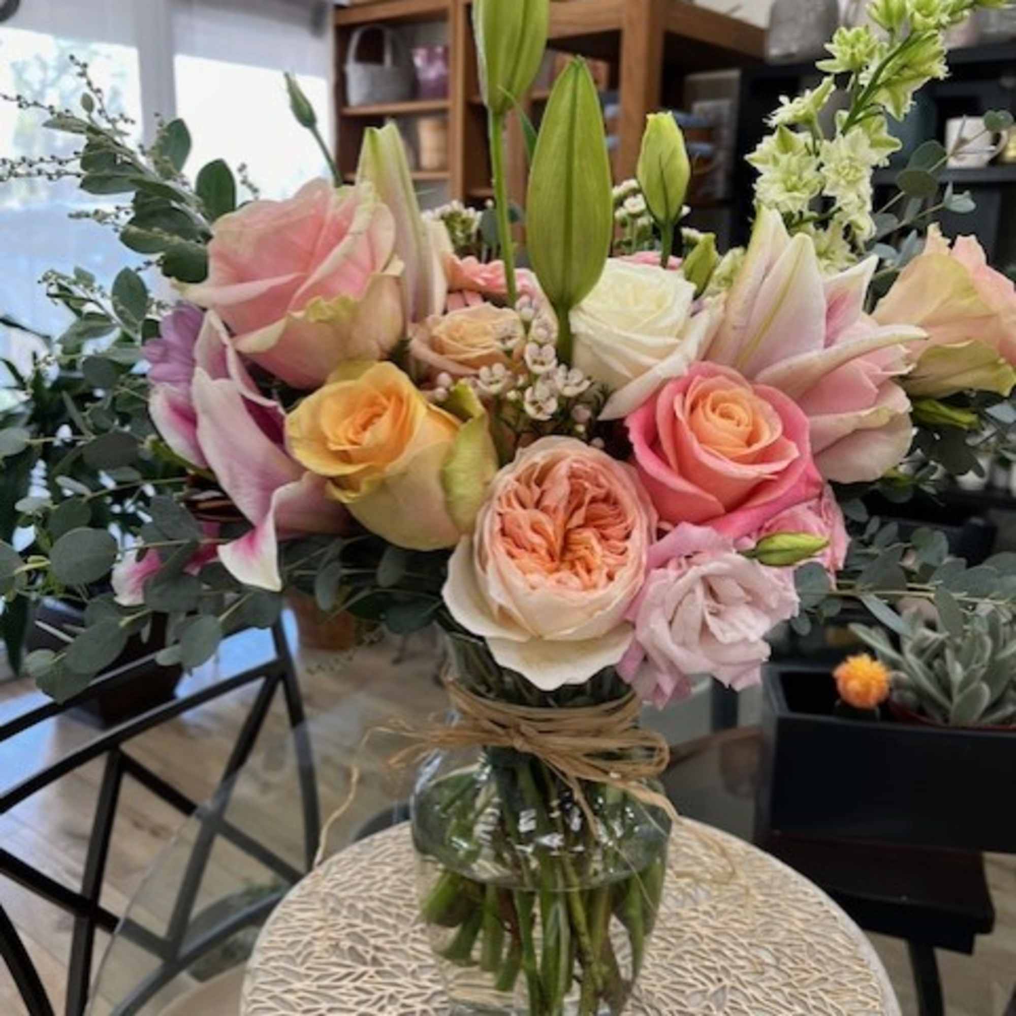 Mixed bouquet of pink roses, lilies, and white blooms in a glass vase