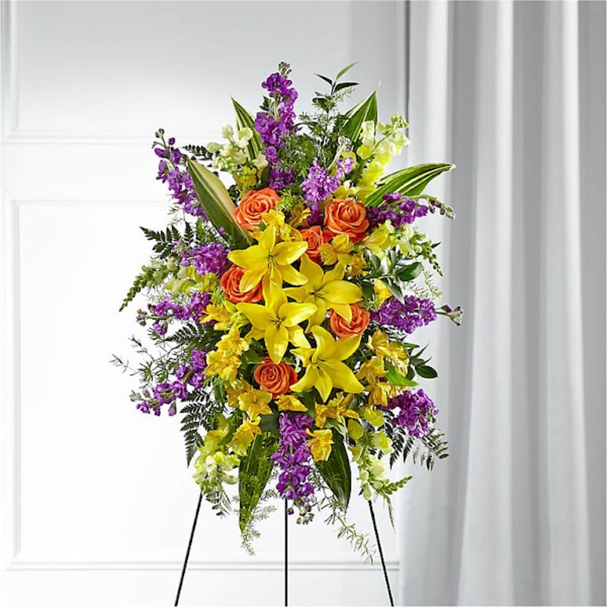 Standing floral spray with yellow lilies, orange roses, and purple flowers
