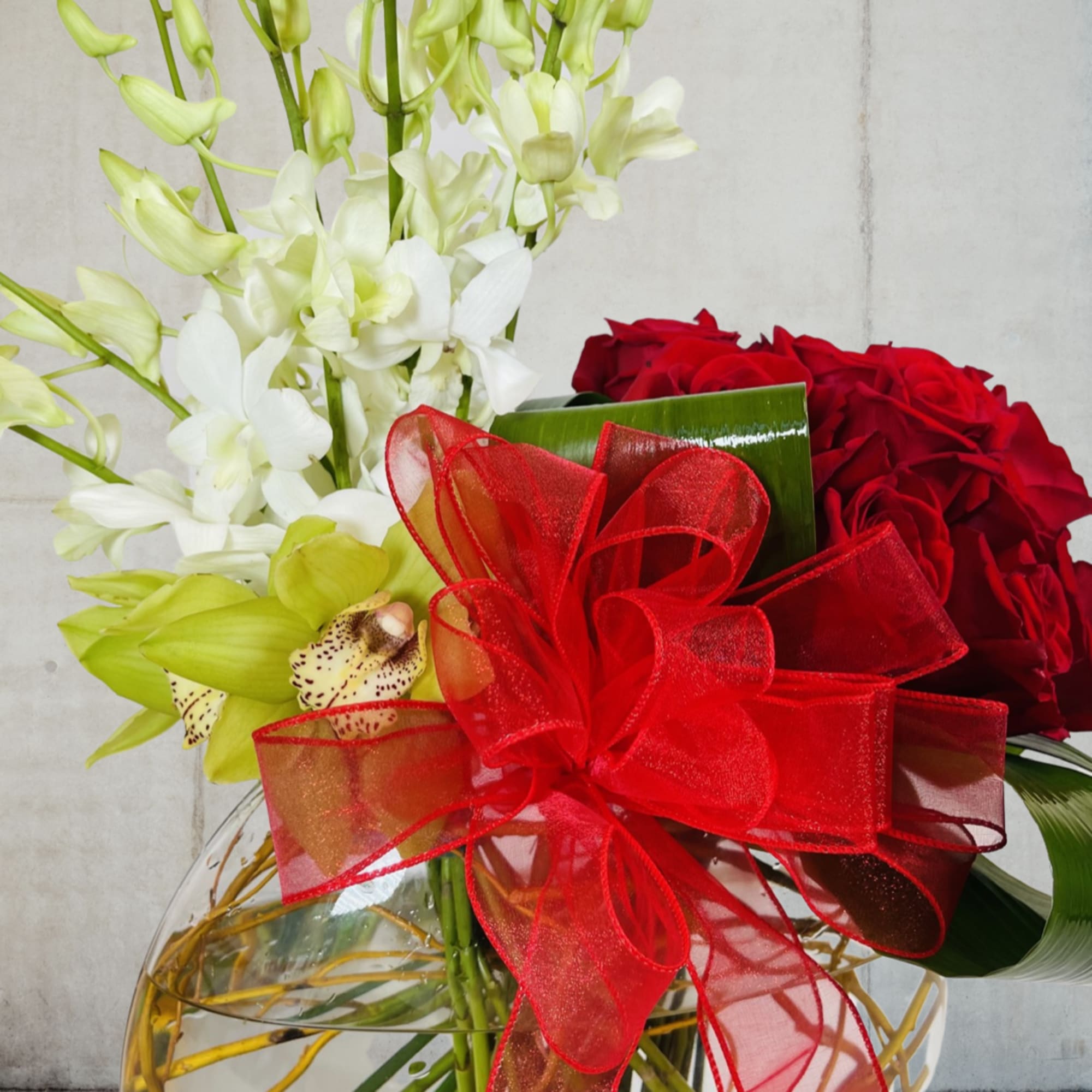 Bouquet of red roses and white orchids with a red ribbon in a glass vase