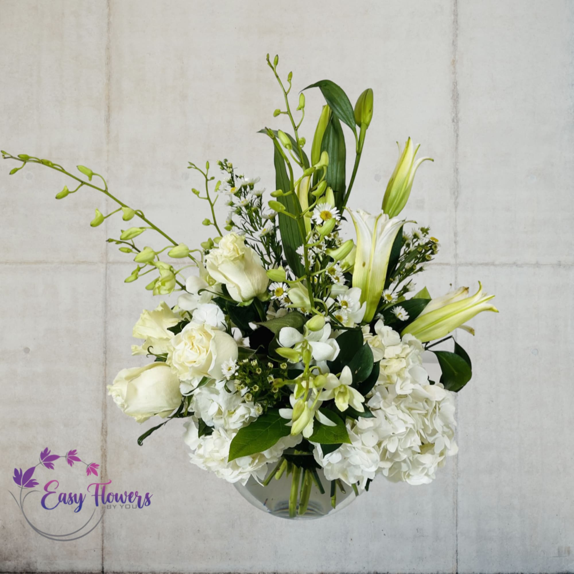 White floral arrangement with lilies, roses, and hydrangeas in a glass vase