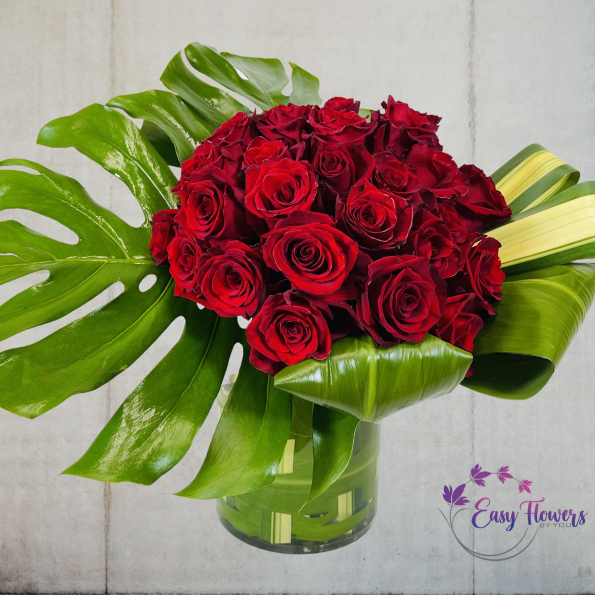 Red roses arranged in a glass vase with large tropical leaves, photo 2 of 2
