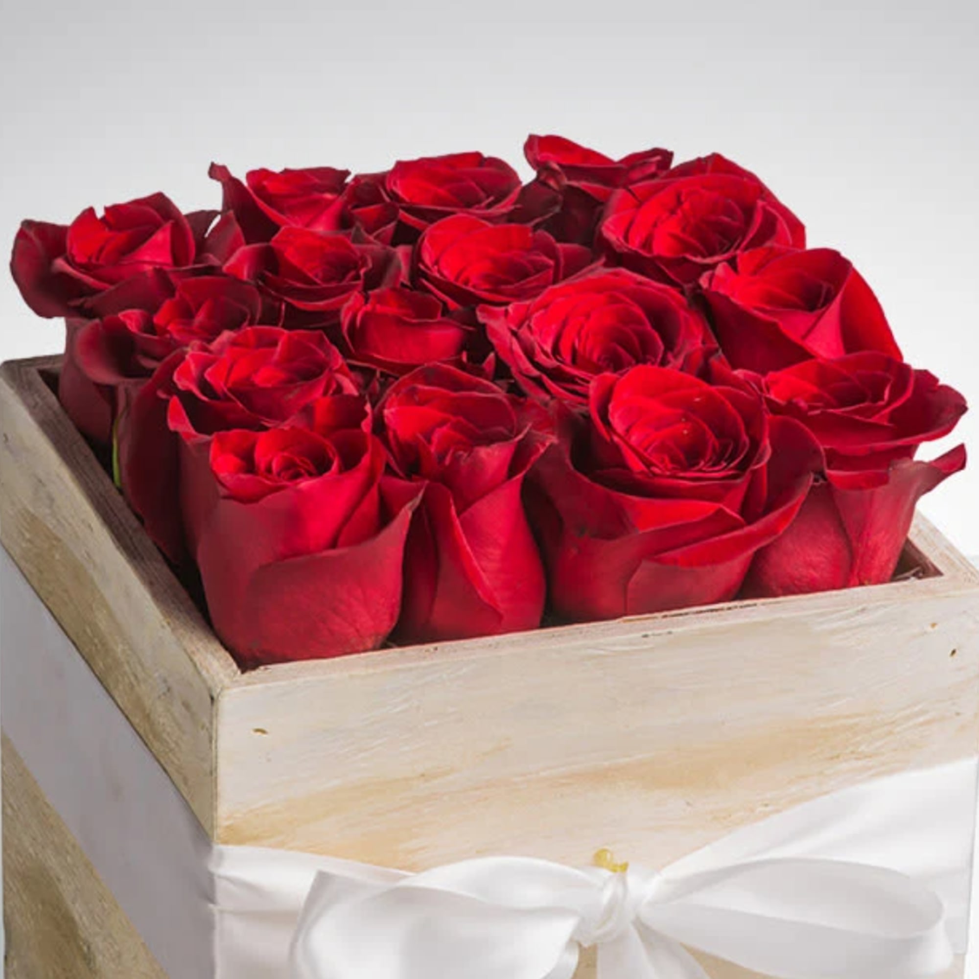 Red roses arranged in a wooden box tied with a white ribbon