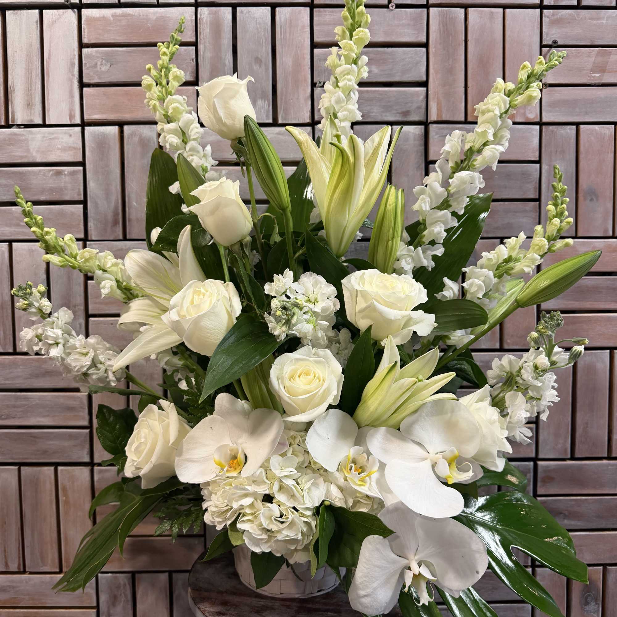 An all-white funeral basket featuring lilies, roses, orchids, and more framed by