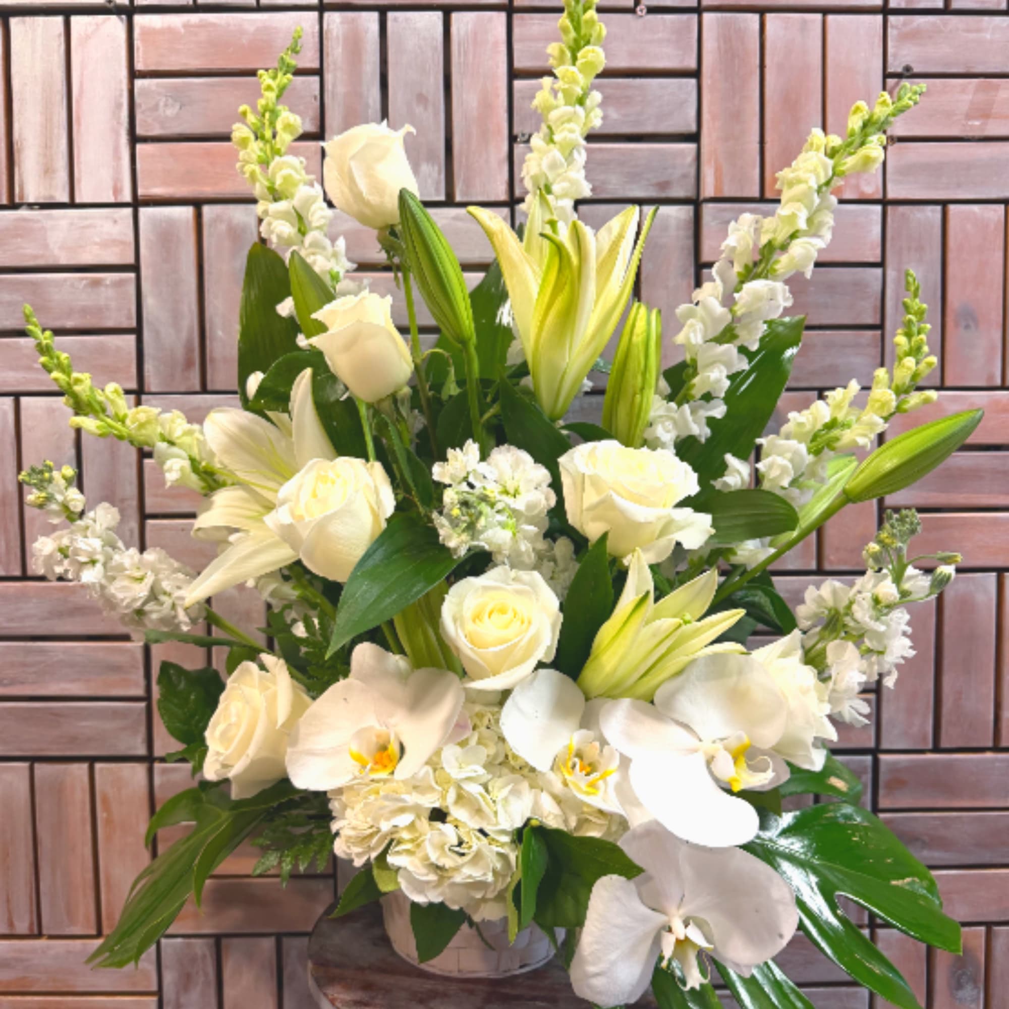 An all-white funeral basket featuring lilies, roses, orchids, and more framed by