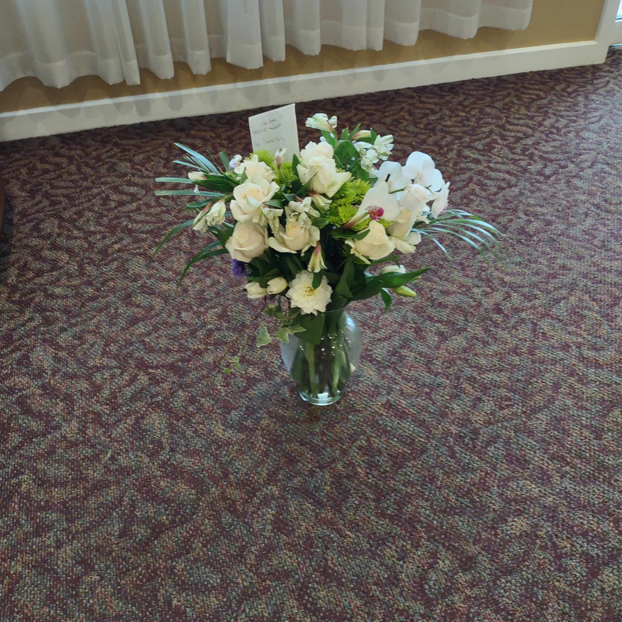 White floral arrangement in a glass vase on carpet