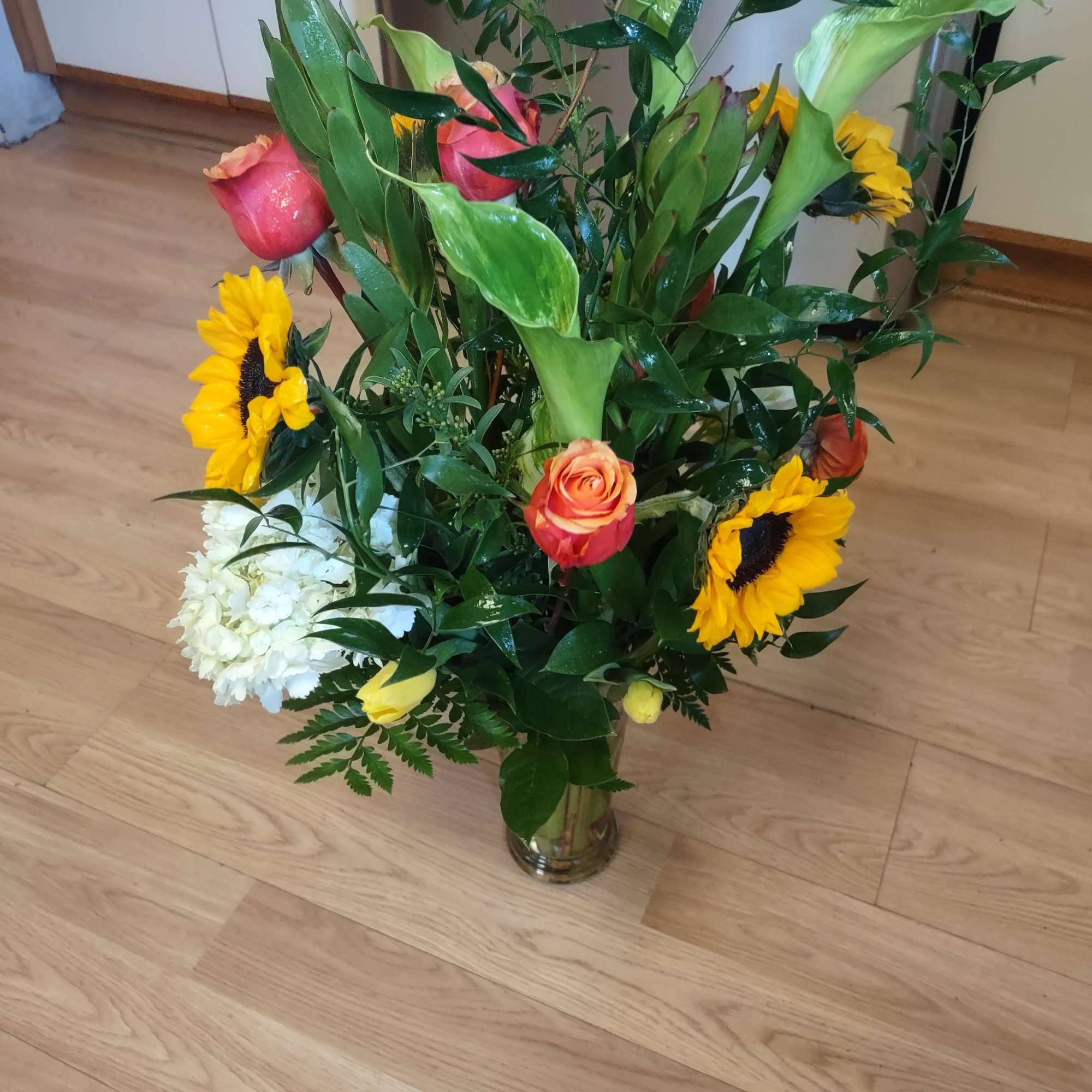 Mixed bouquet with roses, sunflowers, and white blooms in a glass vase