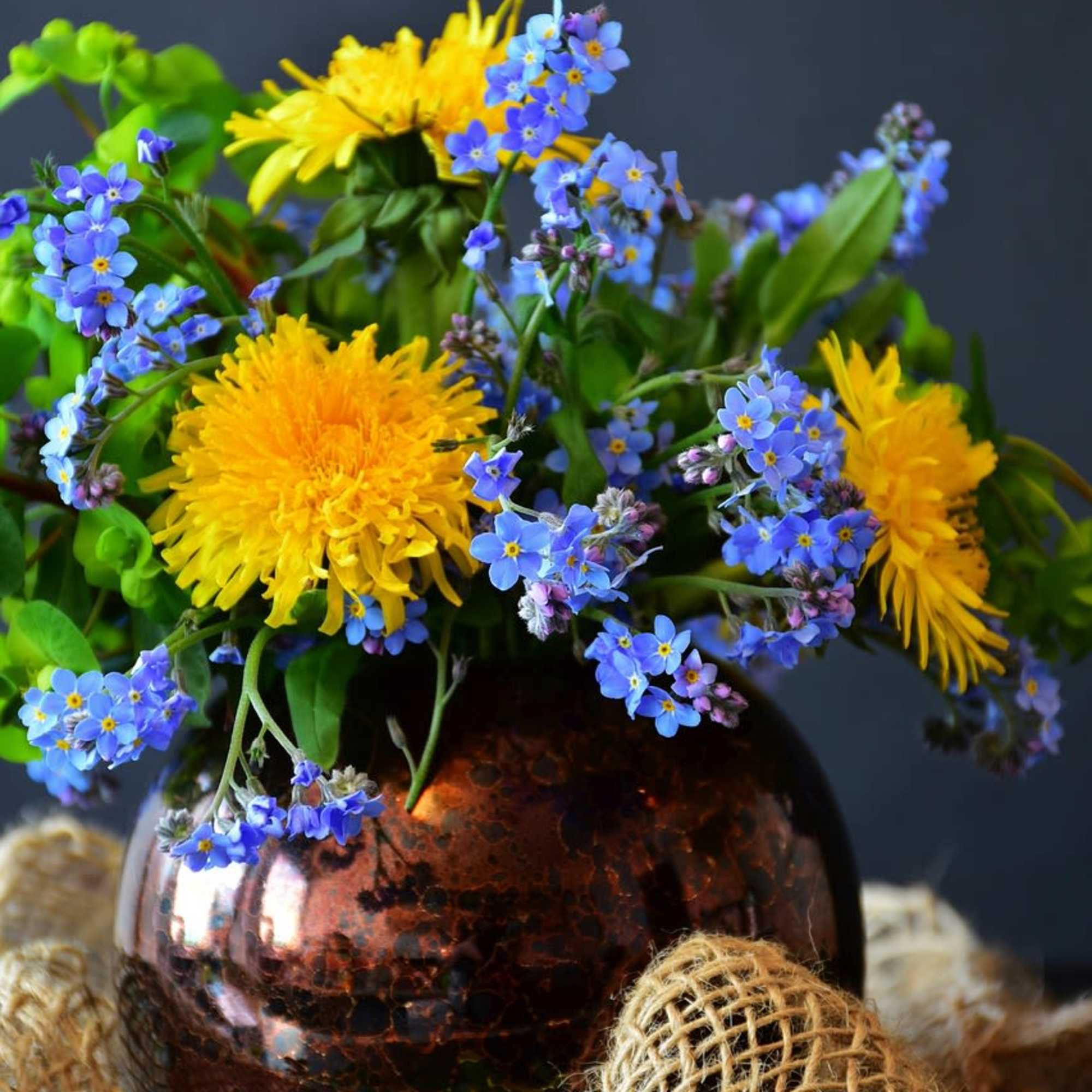 Yellow flowers and blue blossoms arranged in a copper vase