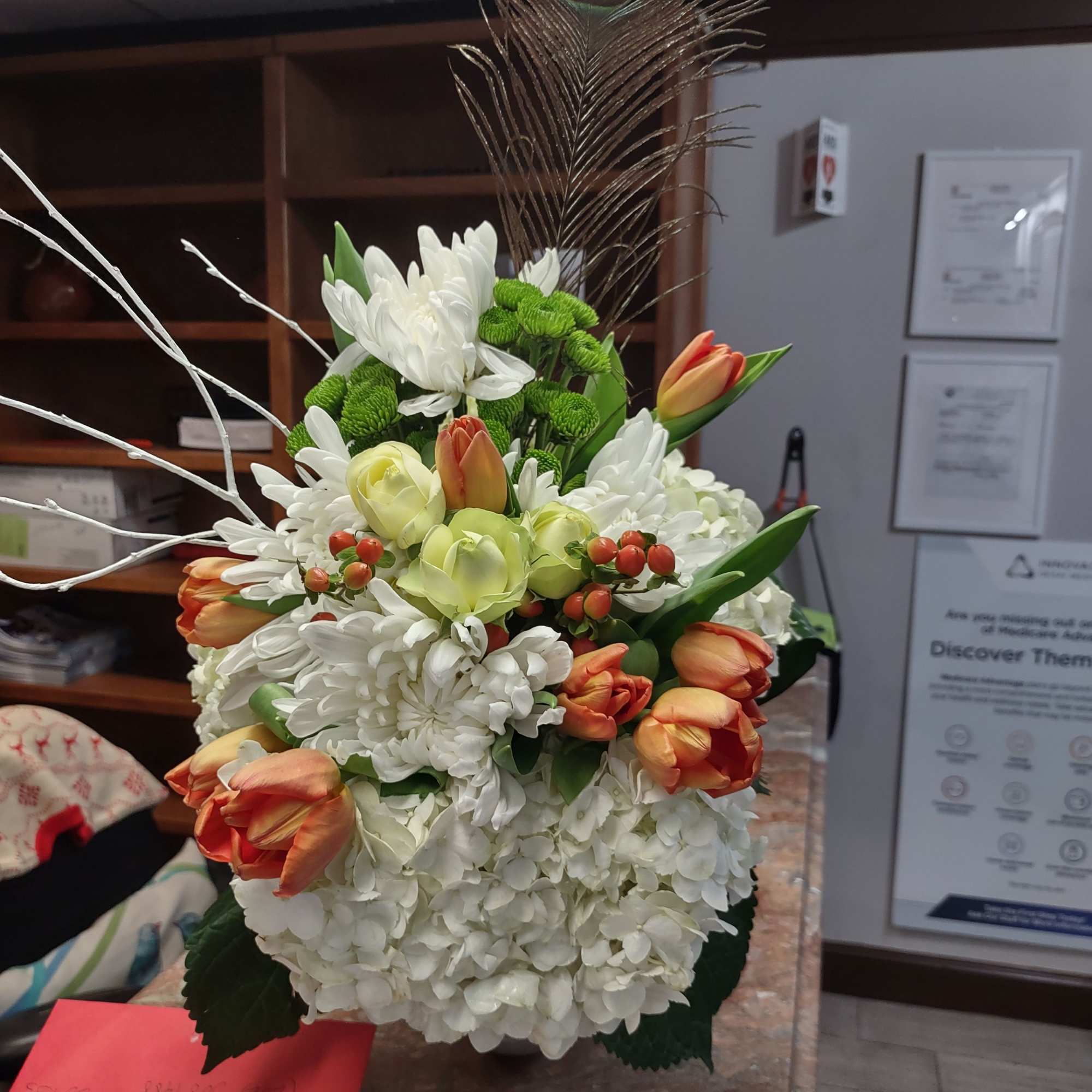 Tall floral arrangement with white blooms, orange tulips, and a peacock feather
