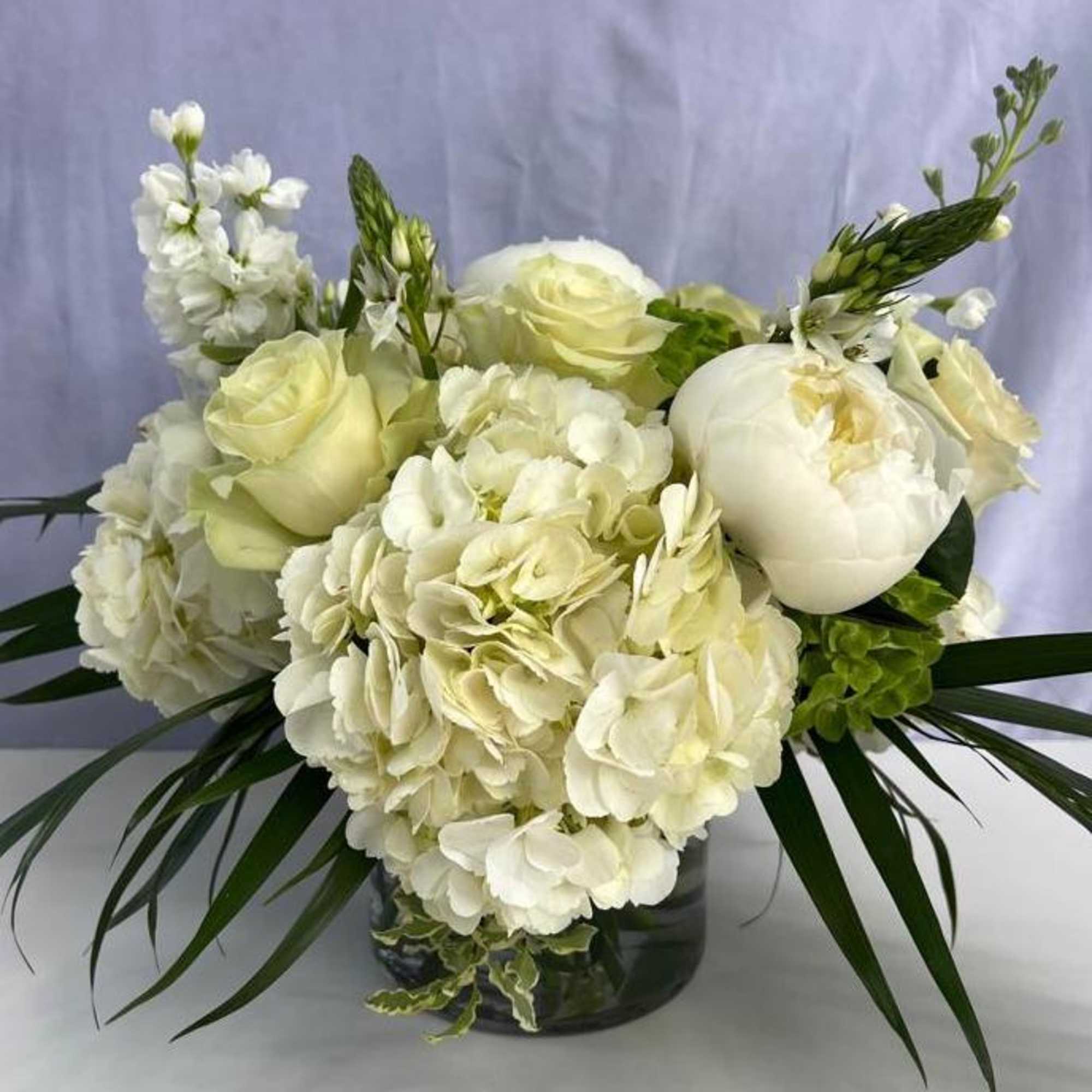Low white arrangement of hydrangeas, roses, and peonies in a clear glass vase