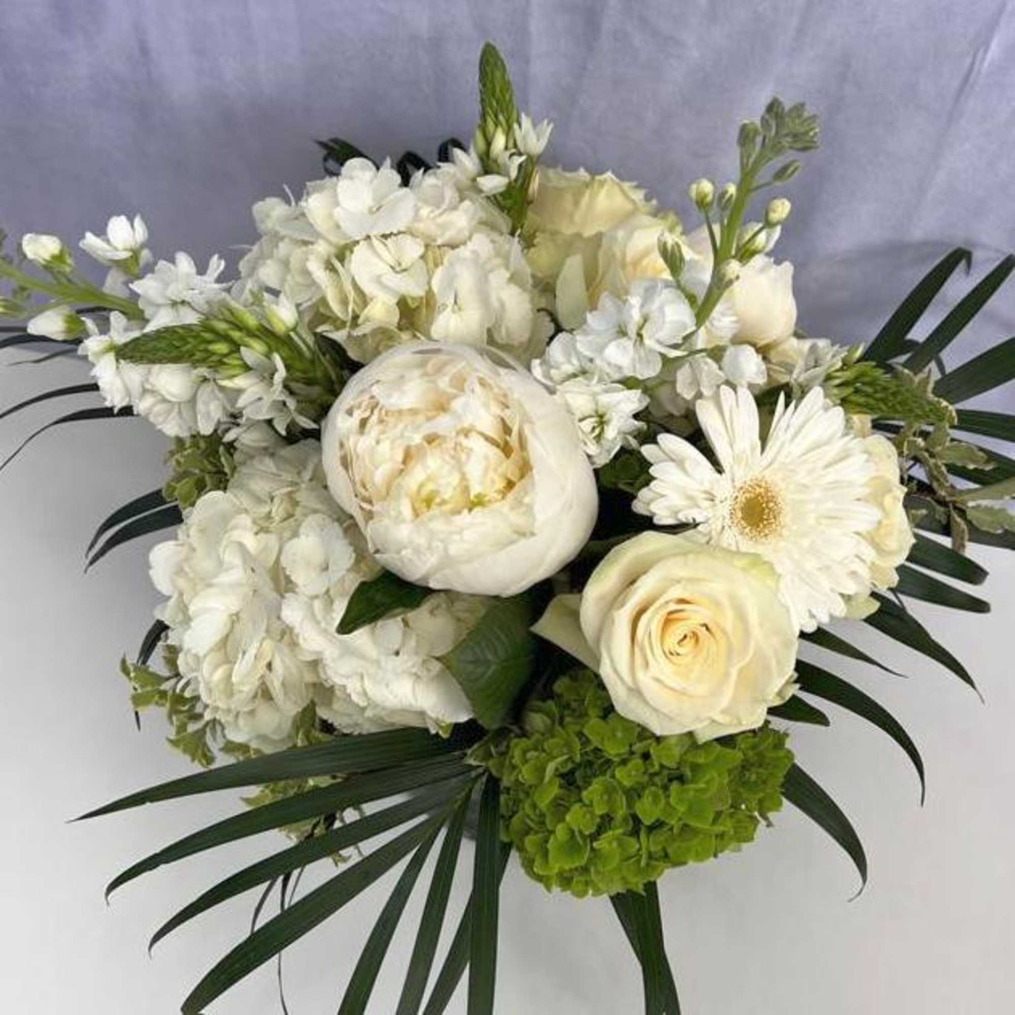 White and cream bouquet with roses, peony, hydrangeas and palm fronds in a compact arrangement.