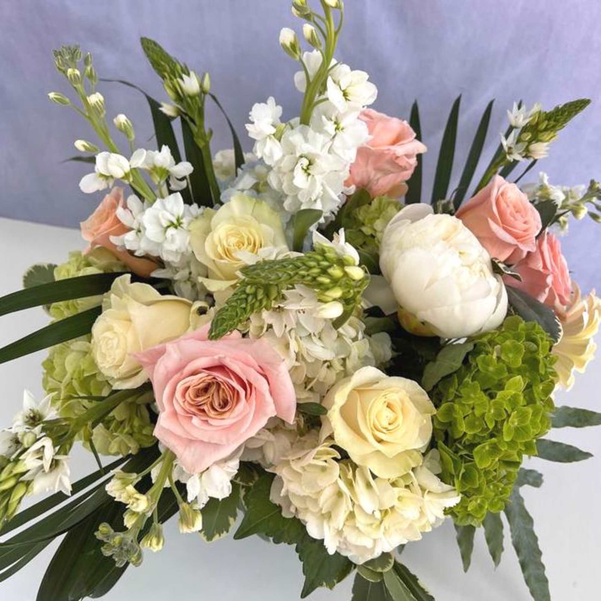 Pastel arrangement of pink and cream roses, white peonies, stock, and hydrangeas in a lush mixed bouquet