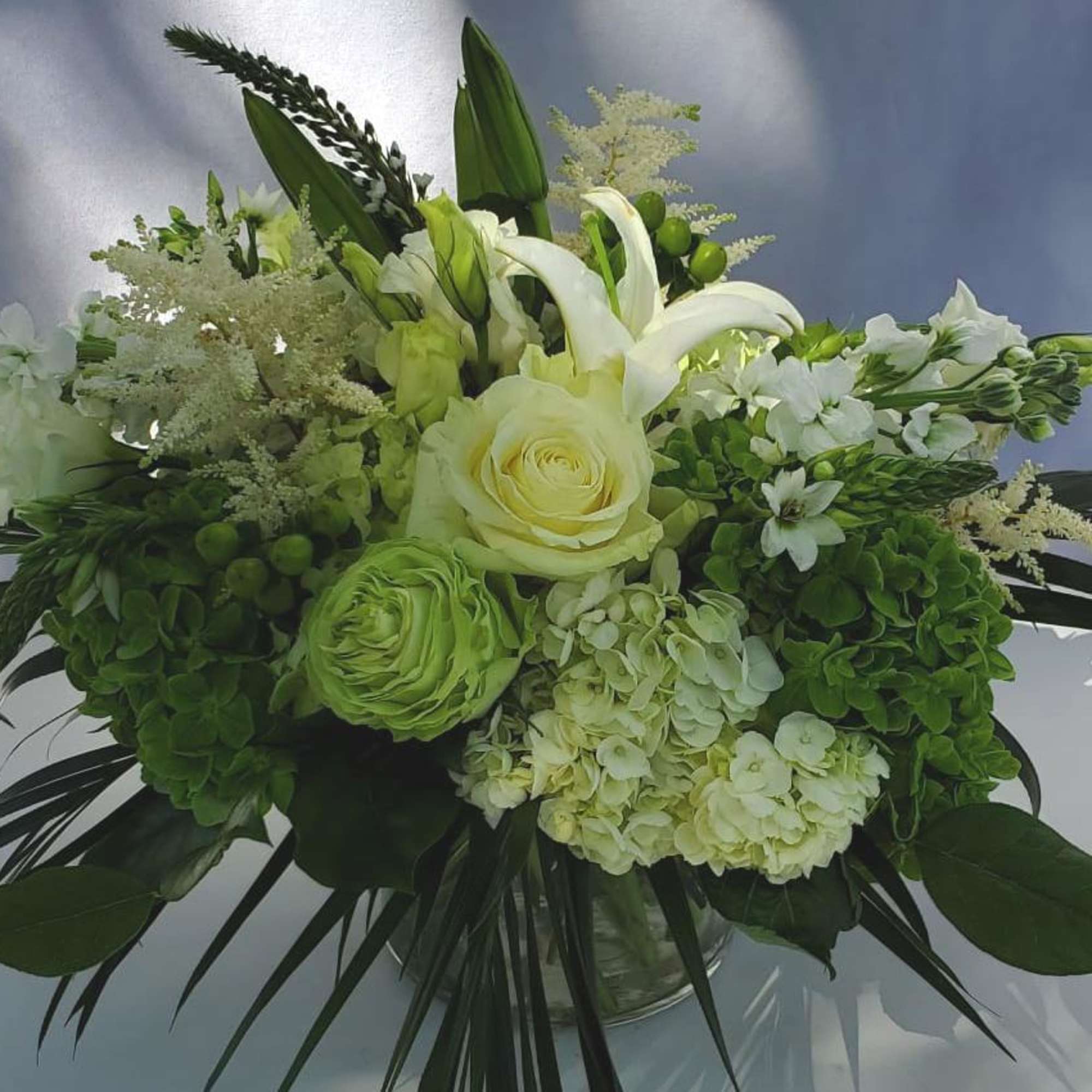 White and green bouquet with roses, lilies, and hydrangeas arranged in a clear glass vase
