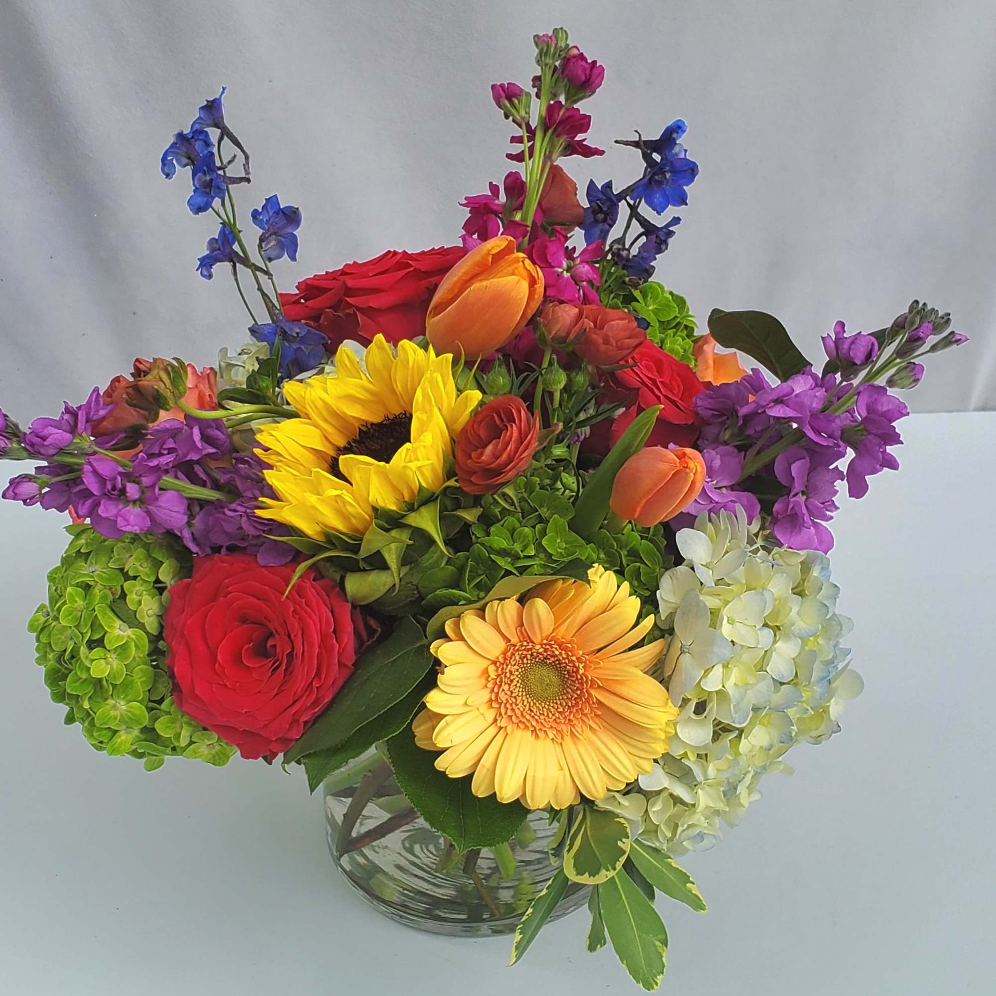 Bright mixed bouquet with sunflowers, roses, tulips, gerbera and hydrangeas in a clear glass vase