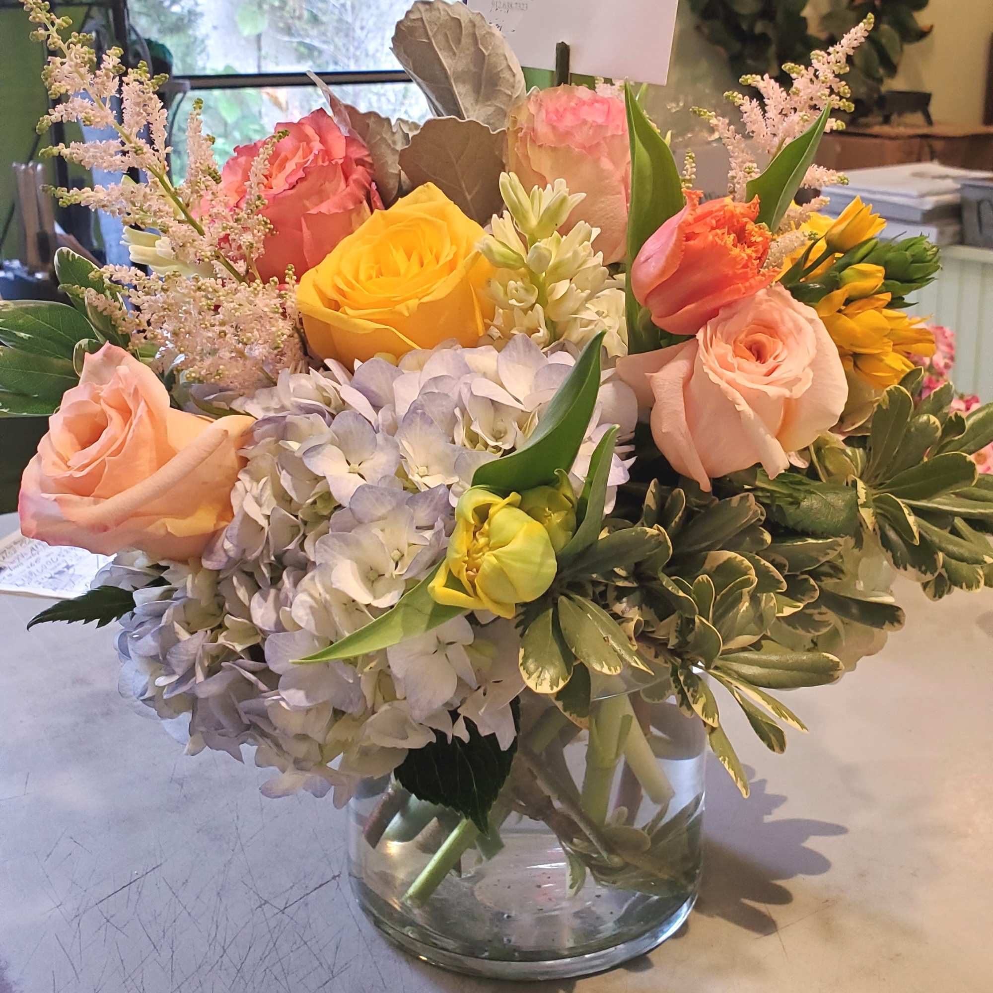 Pastel arrangement of roses, tulips, hydrangea, and mixed blooms in a clear glass vase