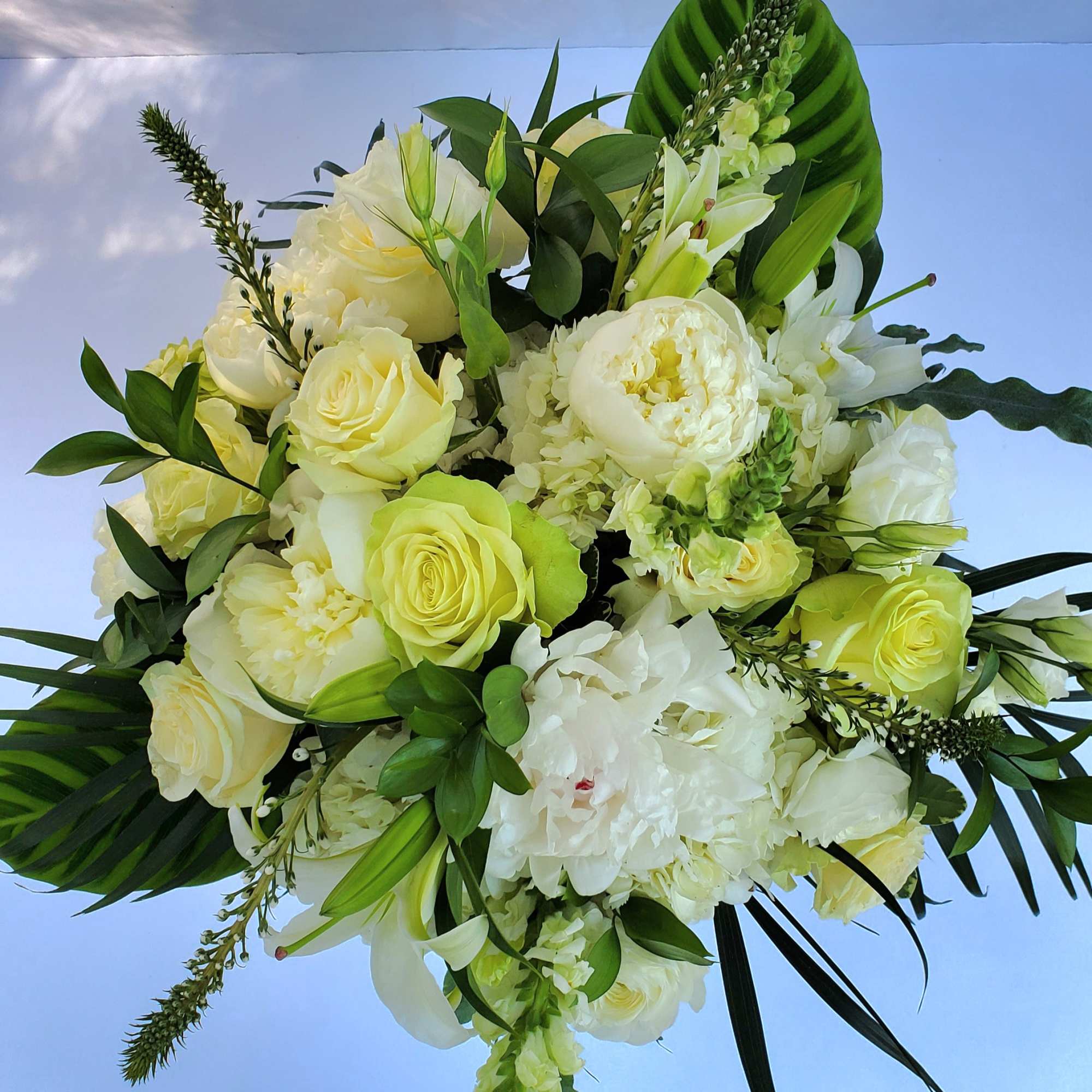 White and pale green roses, peonies, and lilies arranged in a lush white and green bouquet