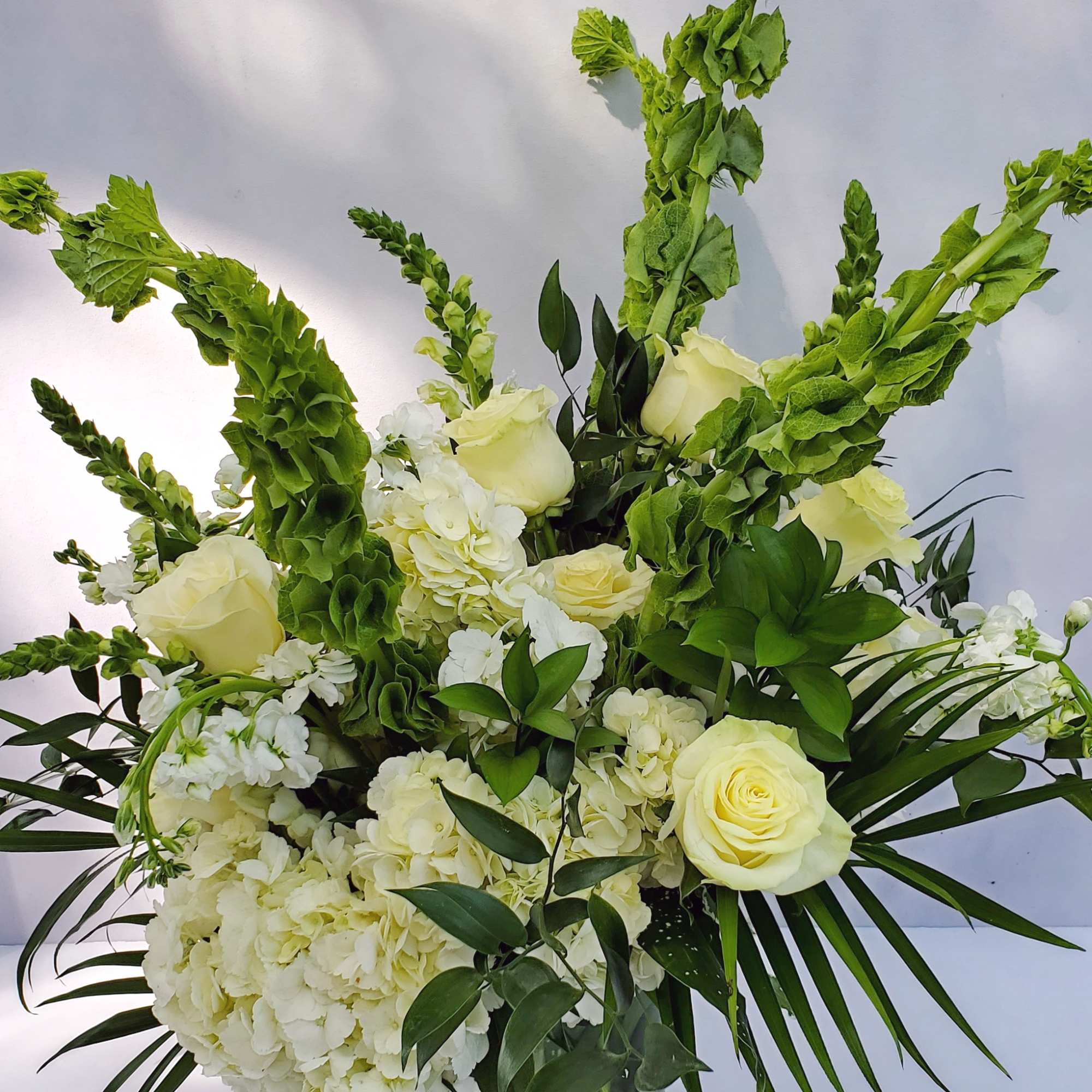 Tall white rose and hydrangea arrangement with green bells of Ireland in a clear glass vase