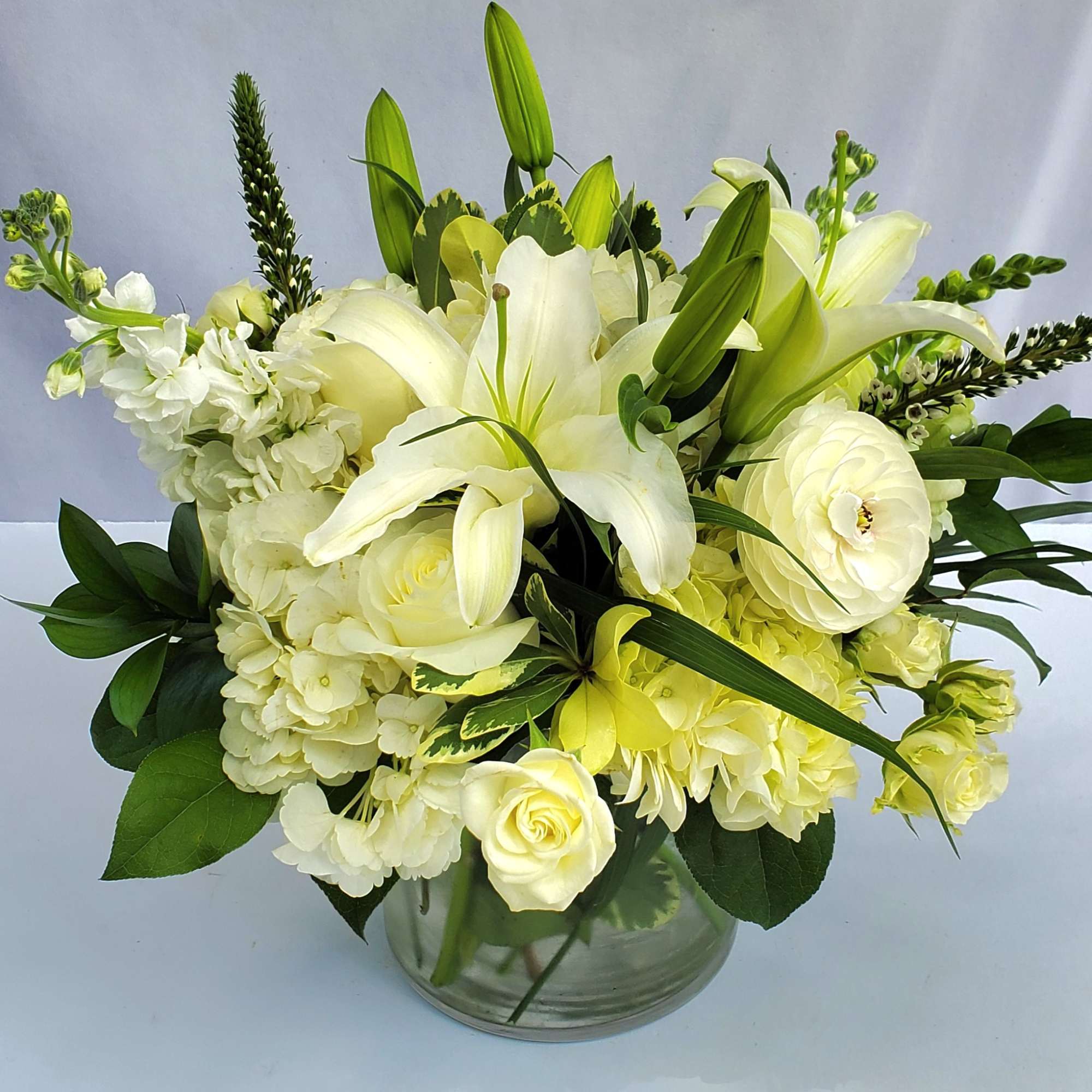 Low arrangement of white lilies, roses, hydrangeas, and ranunculus in a clear glass vase