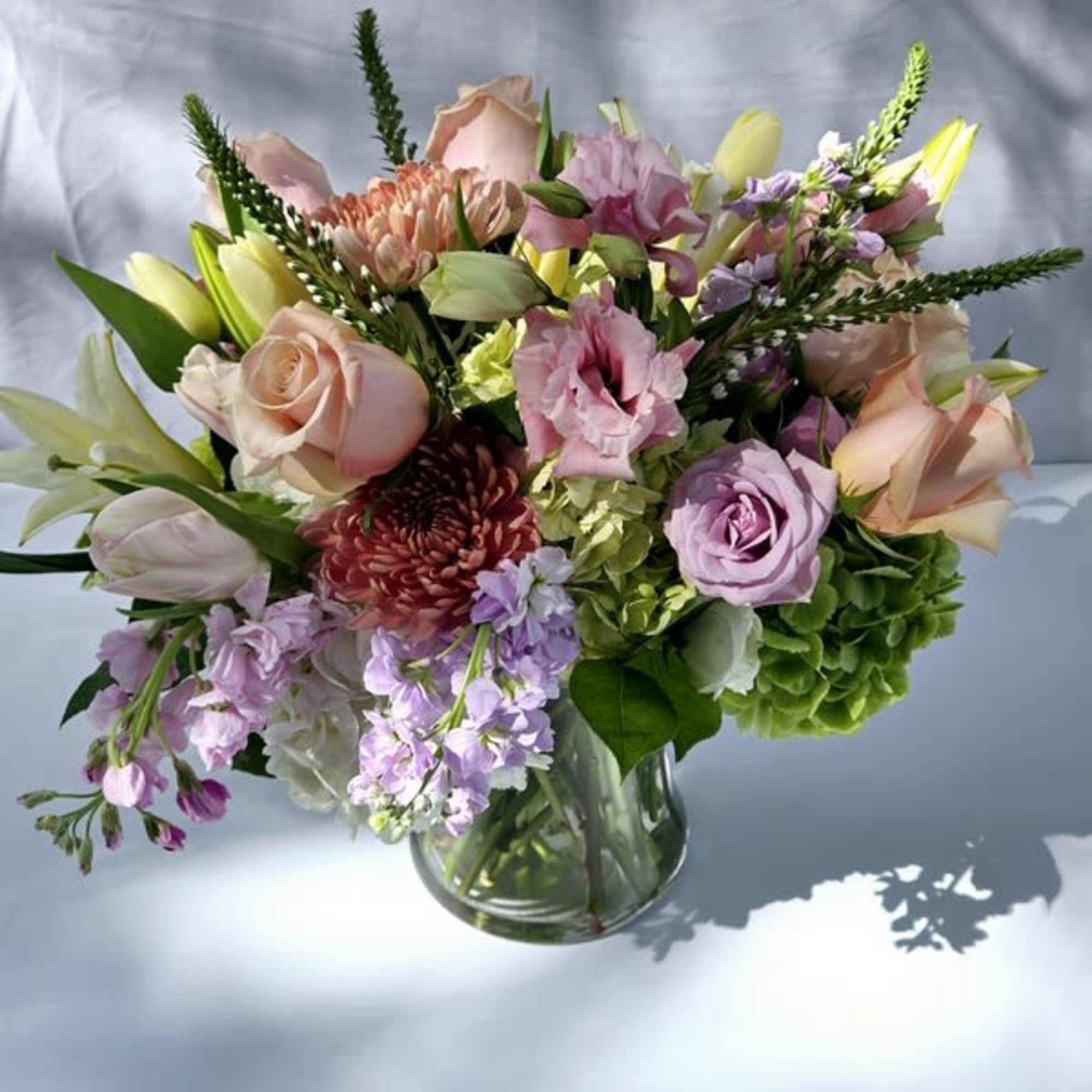 Low glass vase with pastel roses, lilies, hydrangeas and mums in pink, peach, lavender and green tones