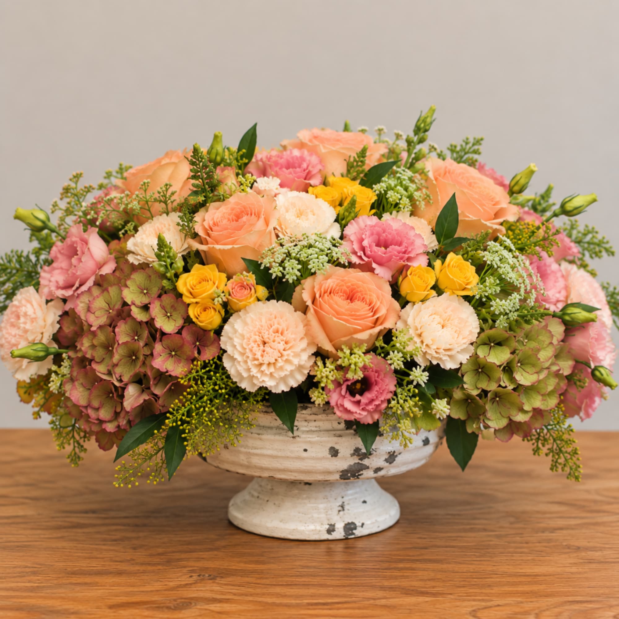 Peach and pink floral arrangement in a white pedestal bowl